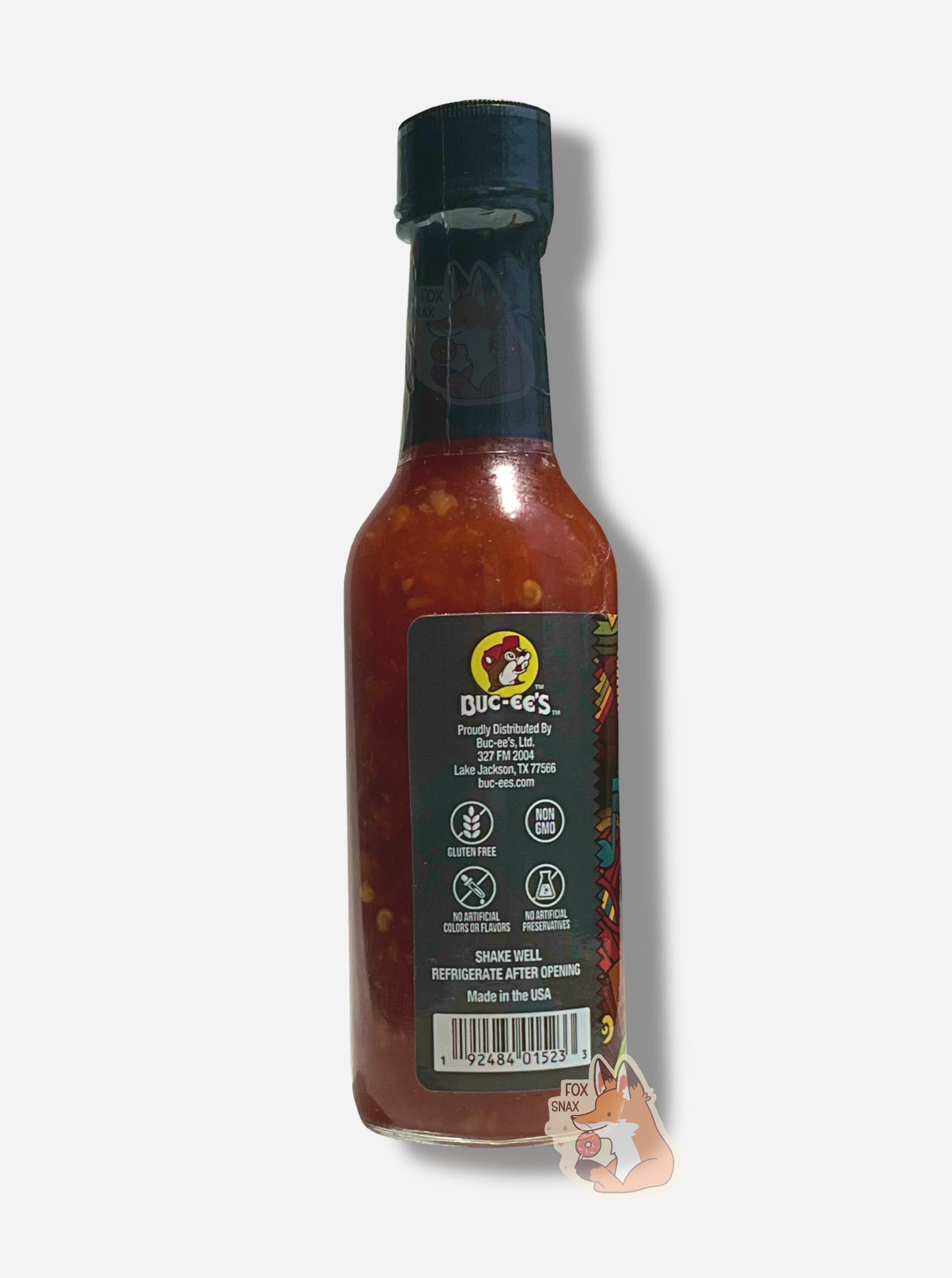 A picture of a small, tall bottle of hot sauce. The top of the bottle is sealed with a shiny green plastic top. The back reads GLUTEN FREE, NON GMO, NO ARTIFICIAL COLORS OR FLAVORS, NO ARTIFICIAL PRESERVATIVES, then SHAKE WELL and REFRIGERATE AFTER OPENING. Made in the USA. The sauce inside is dark red.