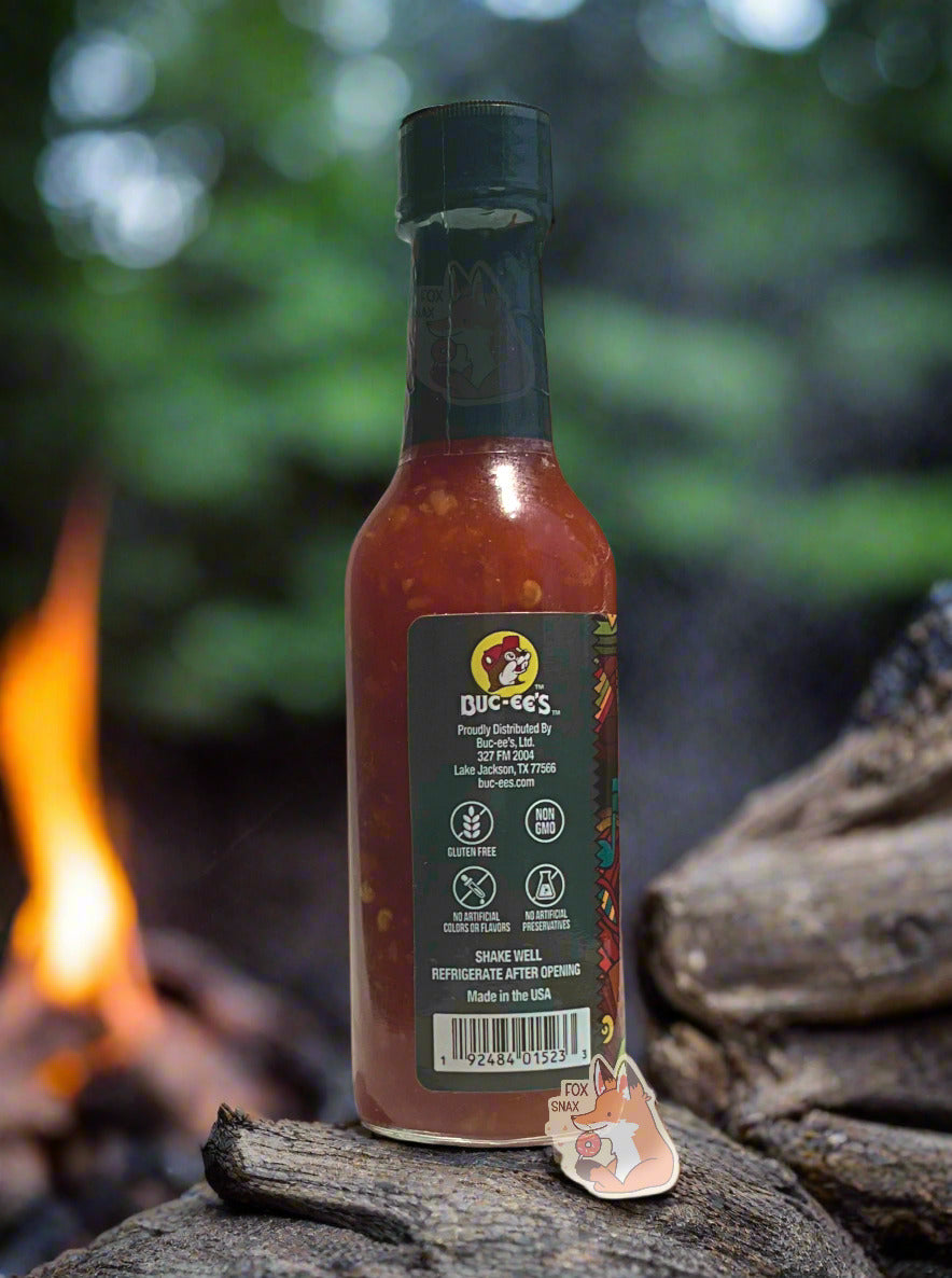 The bottle is sitting on a log; a large campground fire can be seen in the background.