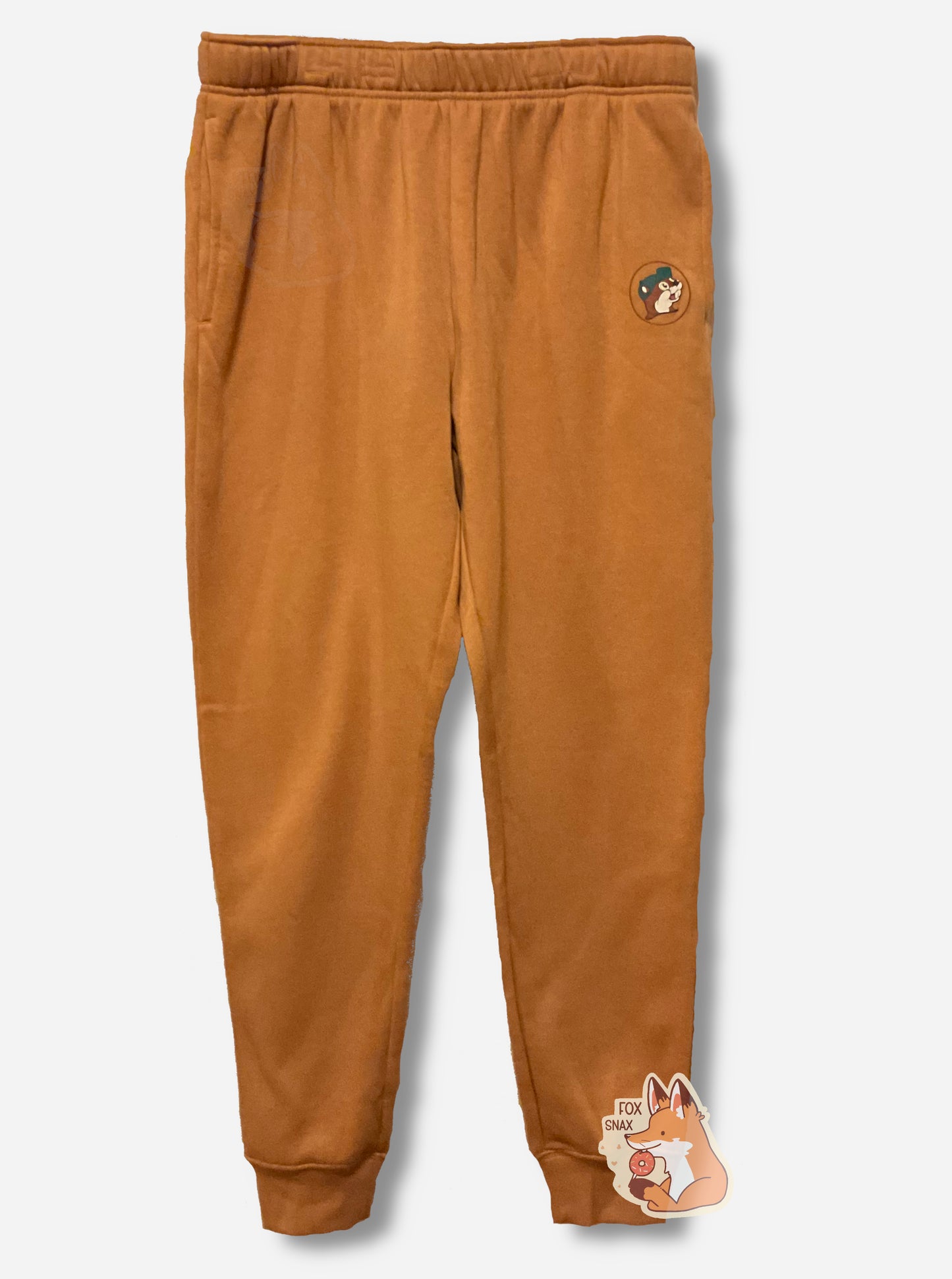A picture of the front of a pair of tan fleece jogging pants. The left leg has the Buc-ee's logo, with Buc-ee's hat in dark blue.