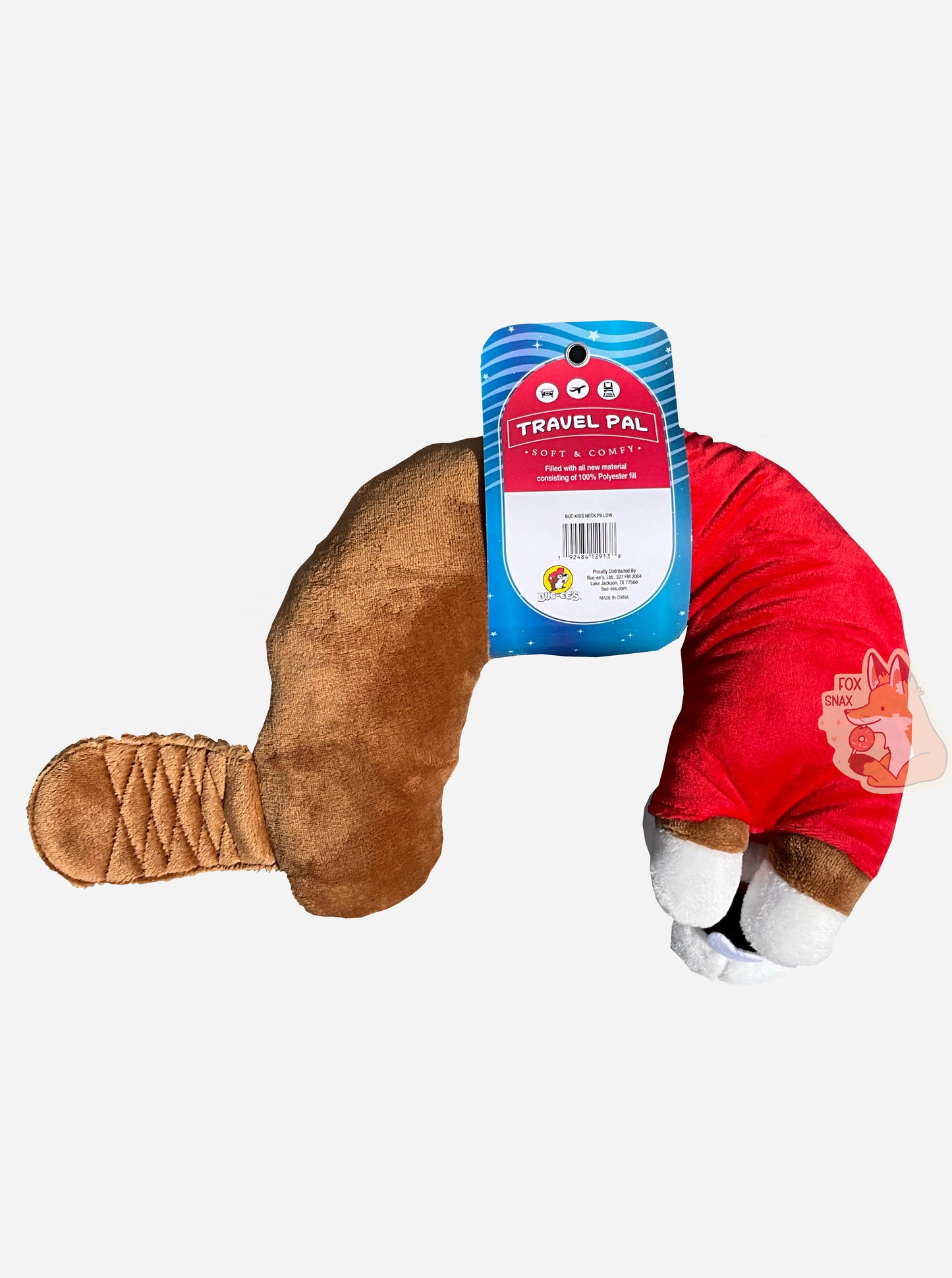 A picture of the bottom of a mostly u-shaped, travel pal pillow. It is is shaped roughly like Buc-ee the Beaver. Buc-ee is wearing a red ball cap, a red Buc-ee's shirt and sports a brown beaver tail. The paper label around his midsection reads TRAVEL PAL, then SOFT AND COMFY, then FILLED WITH ALL NEW MATERIAL CONSISTING OF 100% POLYESTER FILL.