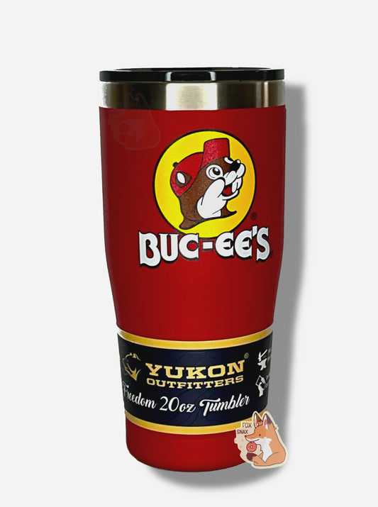 A picture of a tall, red, tumbler, with a big picture of Buc-ee The Beaver on it.  The surface is smooth and red, as it is red paint covering stainless steel.  There is no handle.  The top is plastic.  The top of the mug is lined with a stainless steel band.  A paper wrapper around the bottom reads: Yukon Outfitters.  Freedom 20 oz Tumbler.