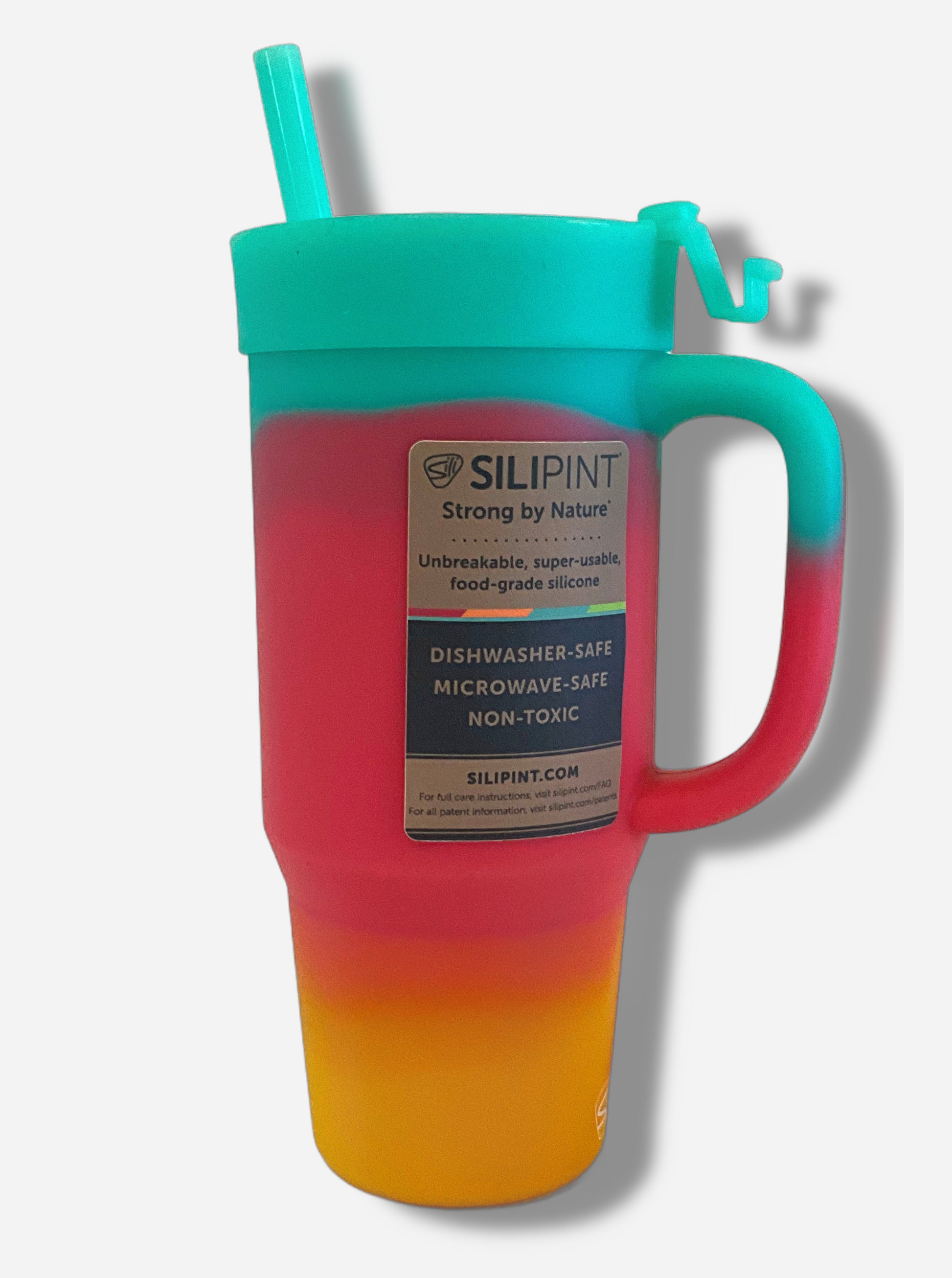 A picture of the back of a tall, rainbow colored tumbler.  The surface starts as orange-yellow on the bottom, fading to red in the middle, then blue/green at the top.  The entire mug is made of silicone, including the top and the straw.  A brown sticker, in black font on the back, reads "SILIPINT, Strong By Nature, Unbreakable, super-usable, food-grade silicone.  Dishwasher-safe, Microwave-safe, Non-toxic.  Silipint.com"