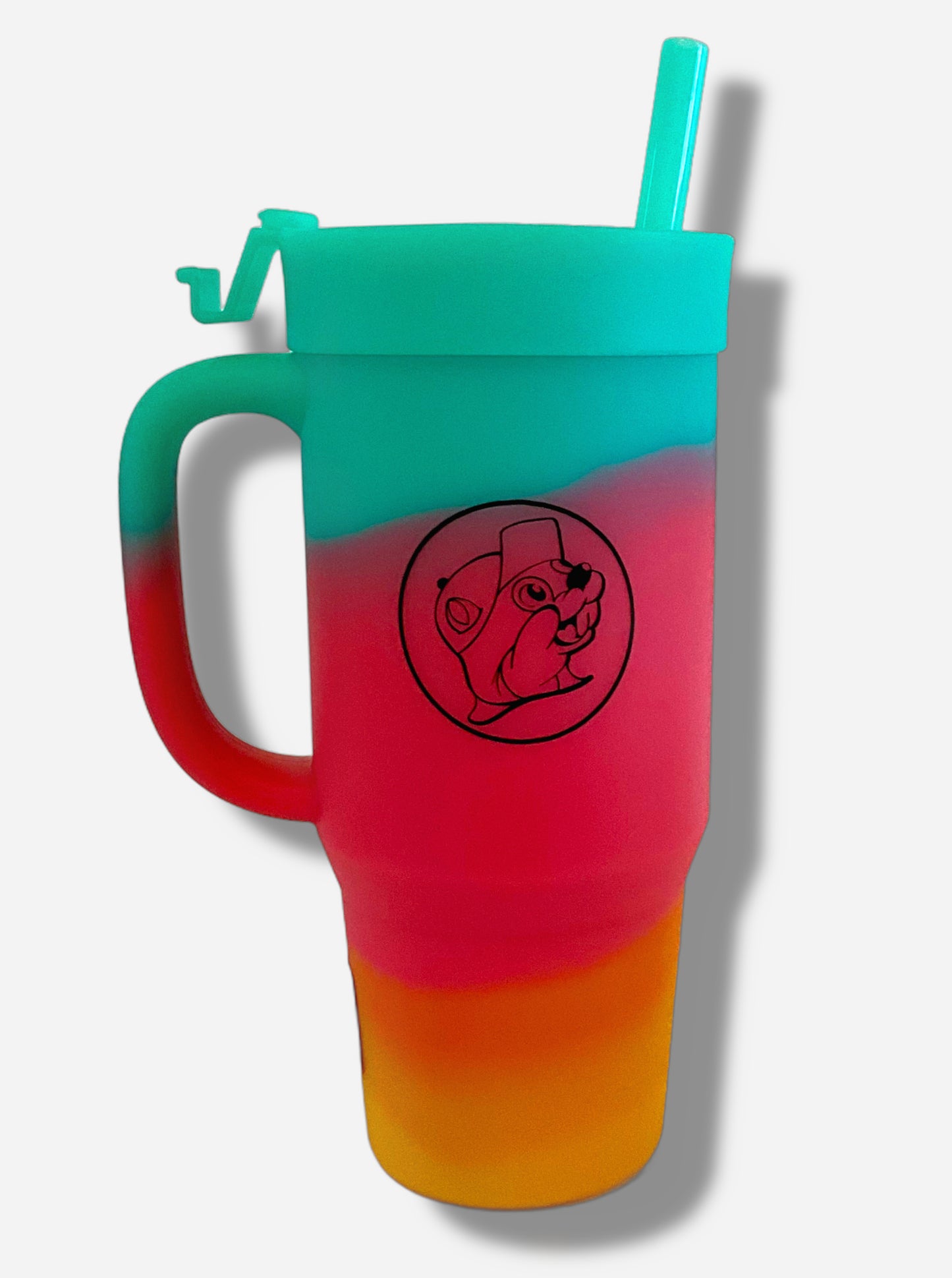 A picture of a tall, rainbow colored tumbler with a big outline of Buc-ee The Beaver on it in black.  The surface starts as orange-yellow on the bottom, fading to red in the middle, then blue/green at the top.  The entire mug is made of silicone, including the top and the straw.