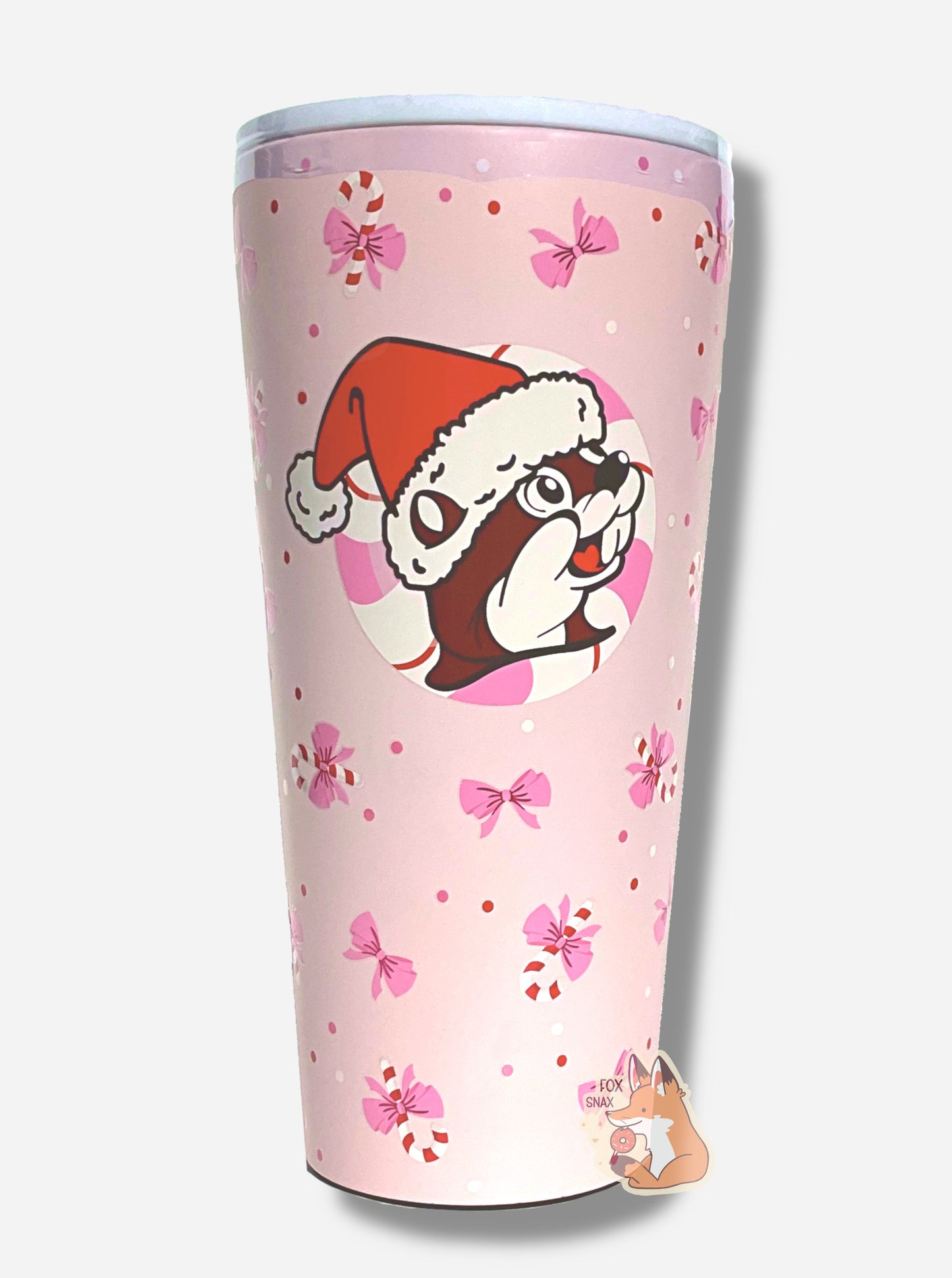 A picture of a pink double pint tumbler, with a light pink background full of bows and candy canes.  The middle of the tumbler has the Buc-ee's logo, but with Buc-ee The Beaver wearing a Santa hat, framed against a red and white peppermint.  The top of the tumbler is white, with a pink slide for different beverage dispenser amounts.  