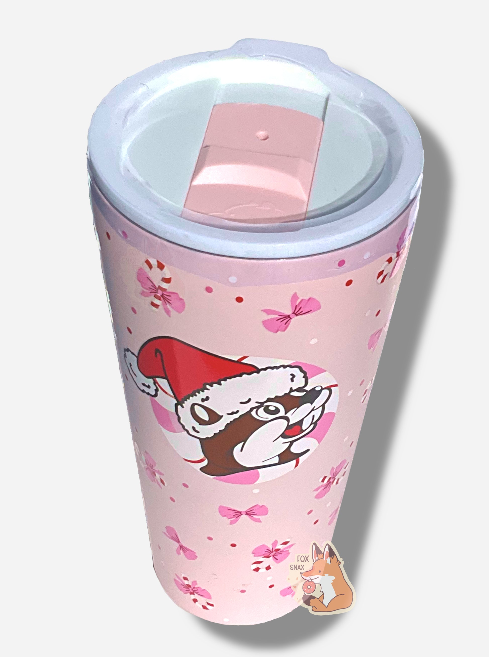 A 3/4 view of a pink double pint tumbler, with a light pink background full of bows and candy canes.  The middle of the tumbler has the Buc-ee's logo, but with Buc-ee The Beaver wearing a Santa hat, framed against a red and white peppermint.  The top of the tumbler is white, with a pink slide for different beverage dispenser amounts.  The label on the bottom reads YUKON OUTFITTERS, then DOUBLE PINT 32 OZ