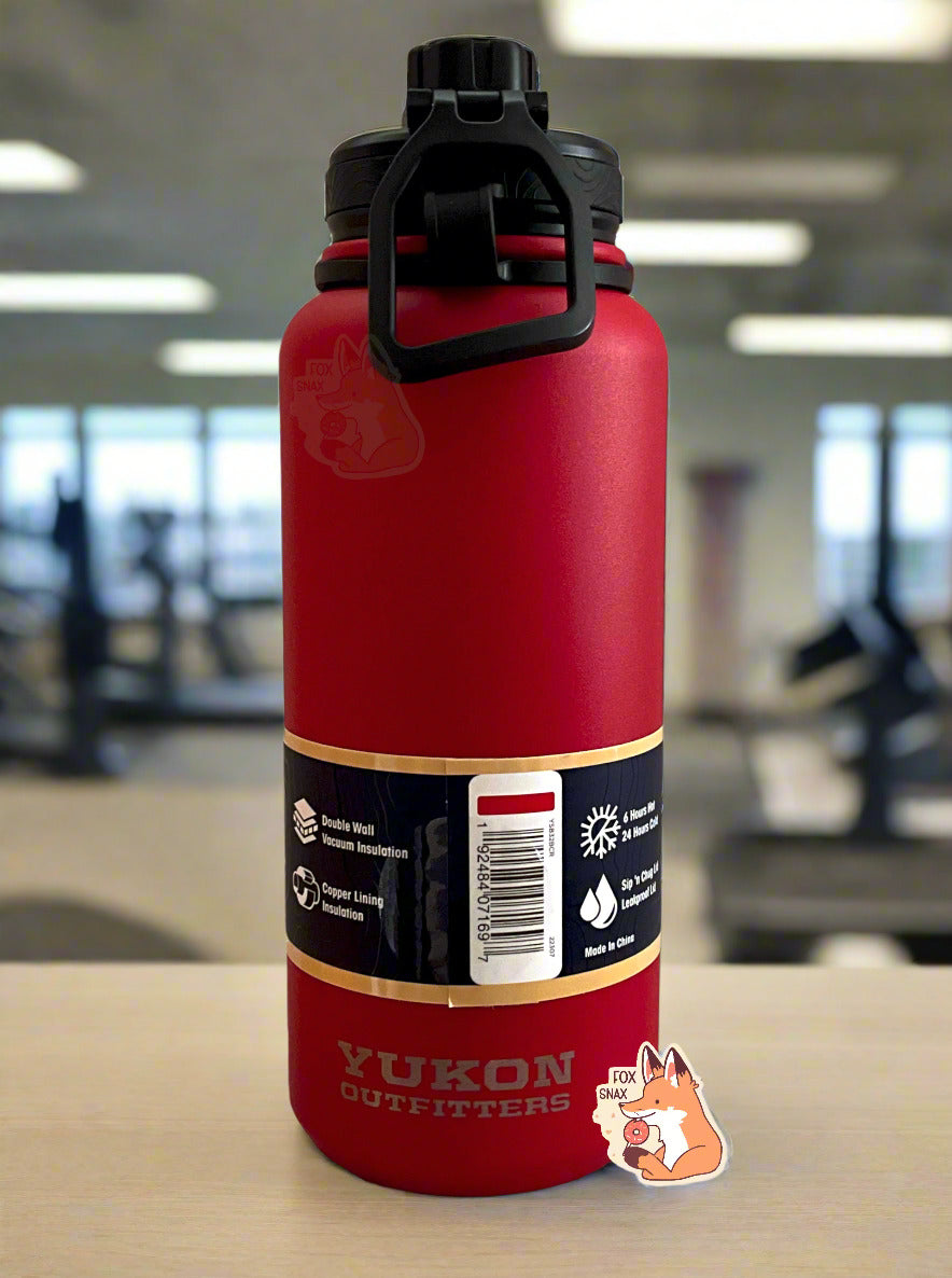 A picture of the back of a tall red cylindrical water bottle.  The surface is smooth and red, as it is red paint covering stainless steel.  There is no handle.  The top is a screw on plastic knob with a keychain handle.  Underneath the paper label, engraved text on the bottom reads: YUKON OUTFITTERS.