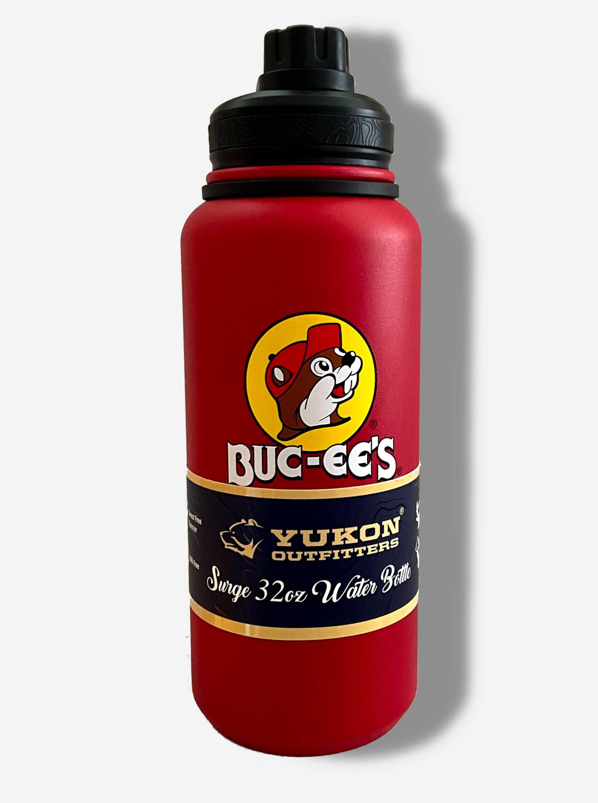 A picture of a tall red cylindrical water bottle, with a big picture of Buc-ee The Beaver on it.  The surface is smooth and red, as it is red paint covering stainless steel.  There is no handle.  The top is a screw on plastic knob with a keychain handle.  A paper wrapper around the bottom reads: Yukon Outfitters.  Surge 32 oz Water Bottle.