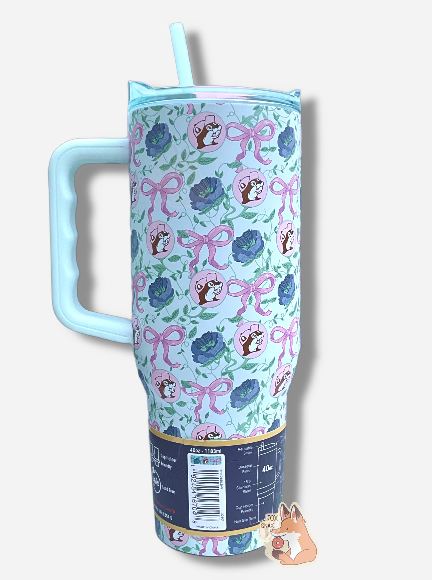 A picture of the back of a tall, light blue, sorta skinny tumbler.  The surface is dotted with Buc-ee's logos, the pink bows, and dark blue flowers.  It is matte paint in covering stainless steel.  The handle, top, and straw are light blue (the top and straw are transparent) and plastic. 