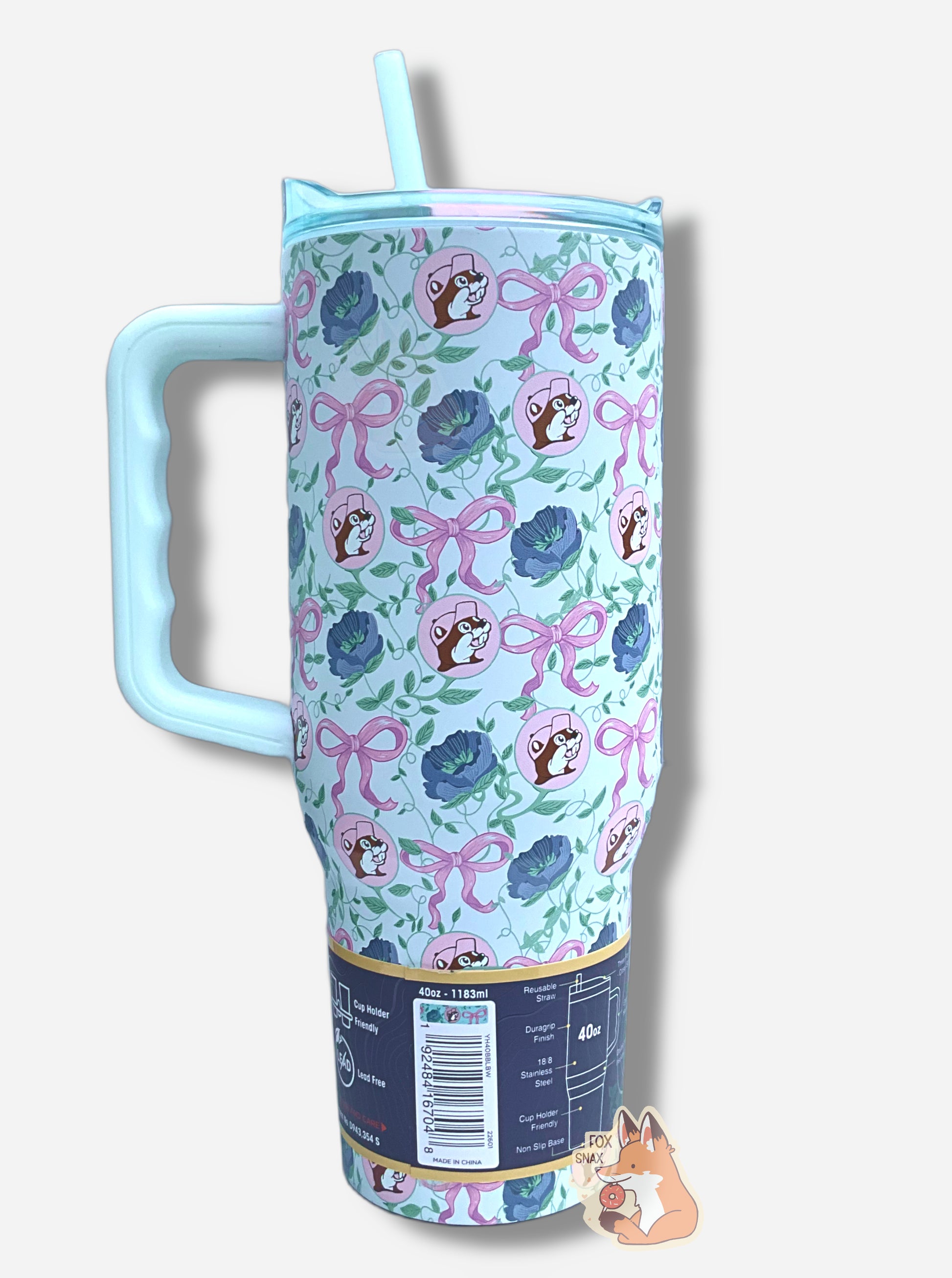 A picture of the back of a tall, light blue, sorta skinny tumbler.  The surface is dotted with Buc-ee's logos, the pink bows, and dark blue flowers.  It is matte paint in covering stainless steel.  The handle, top, and straw are light blue (the top and straw are transparent) and plastic. 