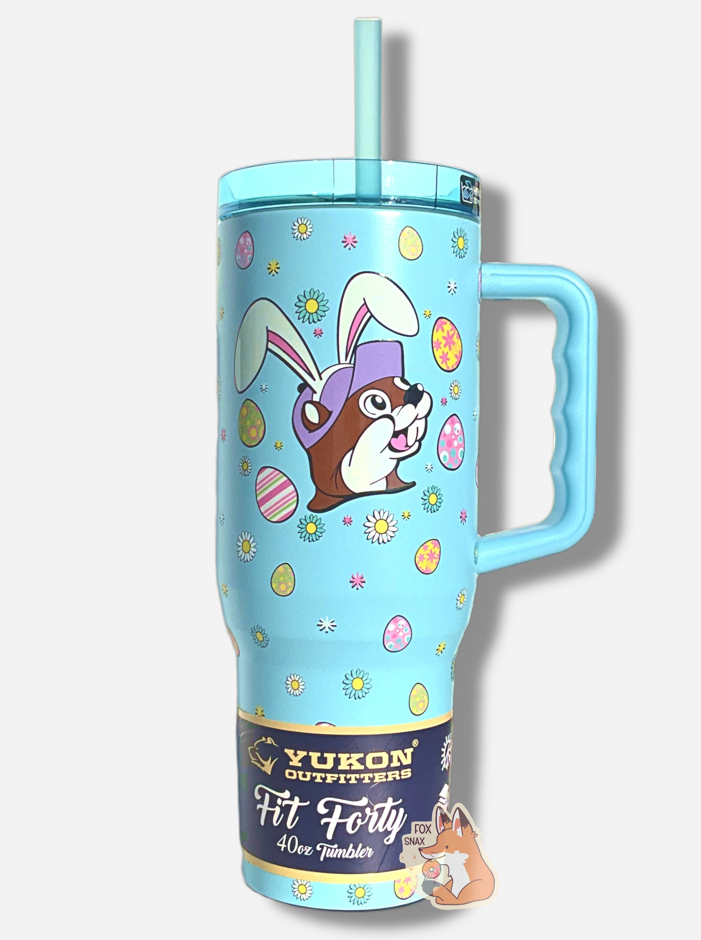 A picture of a tall, light blue, sorta skinny tumbler, with a picture of Buc-ee the Beaver's head, wearing white Easter Bunny ears.  Above and below his head,  are a series of Easter eggs dyed in fantastic patterns and colors, as well as daisy-like flower heads in different petal colors, with a yellow center.  The surface is light blue, as it is paint covering stainless steel.  The top is transparent light  blue  plastic.  The handle is solid light blue  plastic.  The straw is light blue.