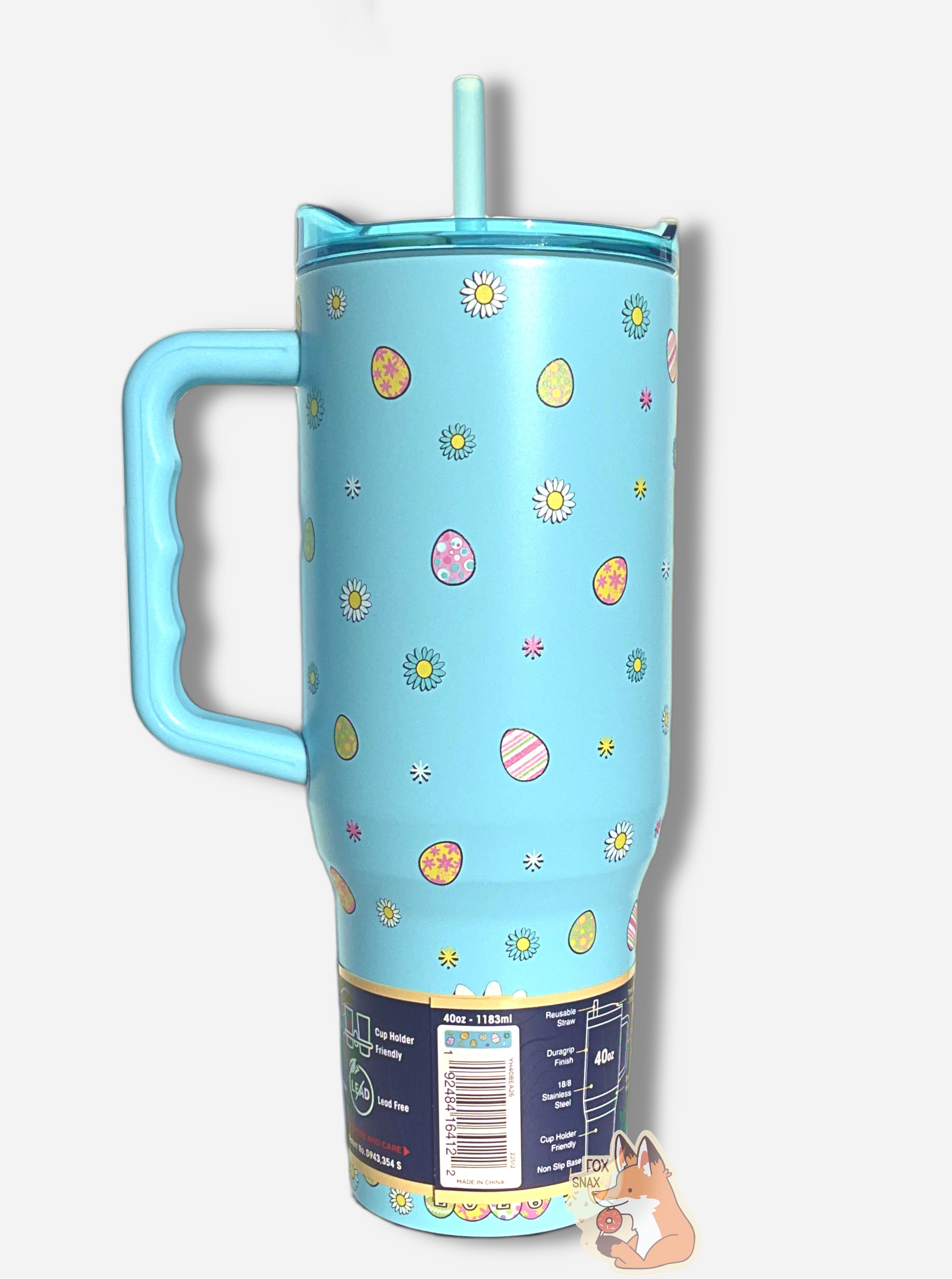 A picture the back of a tall, light blue, sorta skinny tumbler.  On the tumbler are a  series of Easter eggs dyed in fantastic patterns and colors, as well as daisy-like flower heads in different petal colors, with a yellow center.  The surface is light blue, as it is paint covering stainless steel.  The top is transparent light blue plastic.  The bottom of the tumbler reads 2026, with each of the numbers having a background of an Easter egg. The handle is solid light blue plastic.  The straw is light blue.