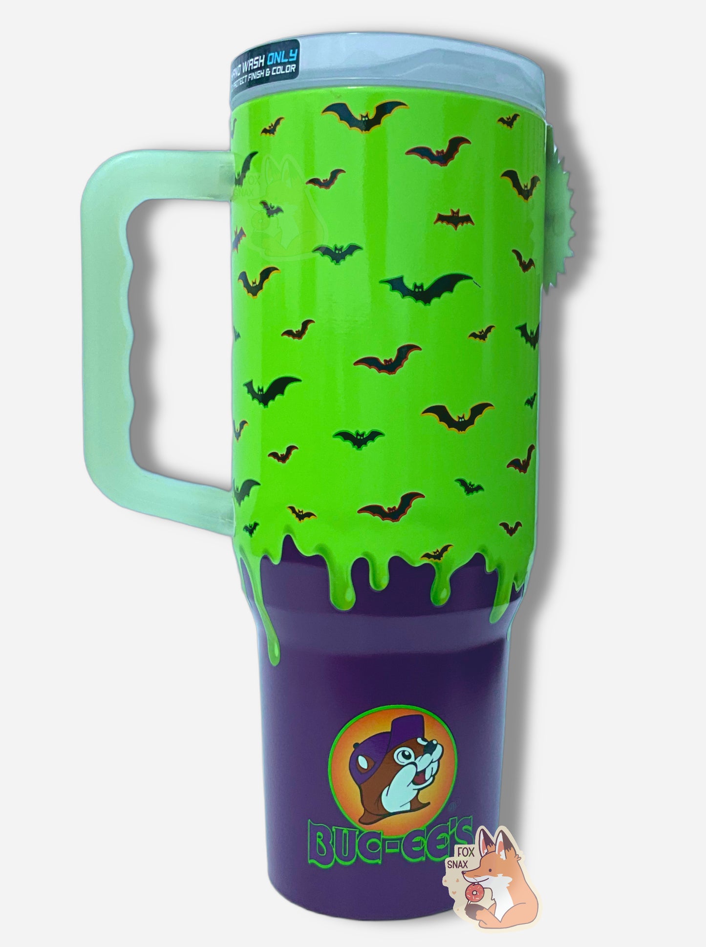 A picture of the back of a tall, green and purple sorta skinny tumbler. The surface  is bright green slime 'dripping' down the tumbler, with black bats against that background.  The bats have purple, green, and yellow outlines.  The bottom fades to solid purple. The tumbler is paint covering stainless steel. The handle and top are glow in the dark plastic.  On the bottom is the Buc-ee's logo, with Buc-ee wearing a purple hat, then BUC-EE'S underneath that in green and purple. 