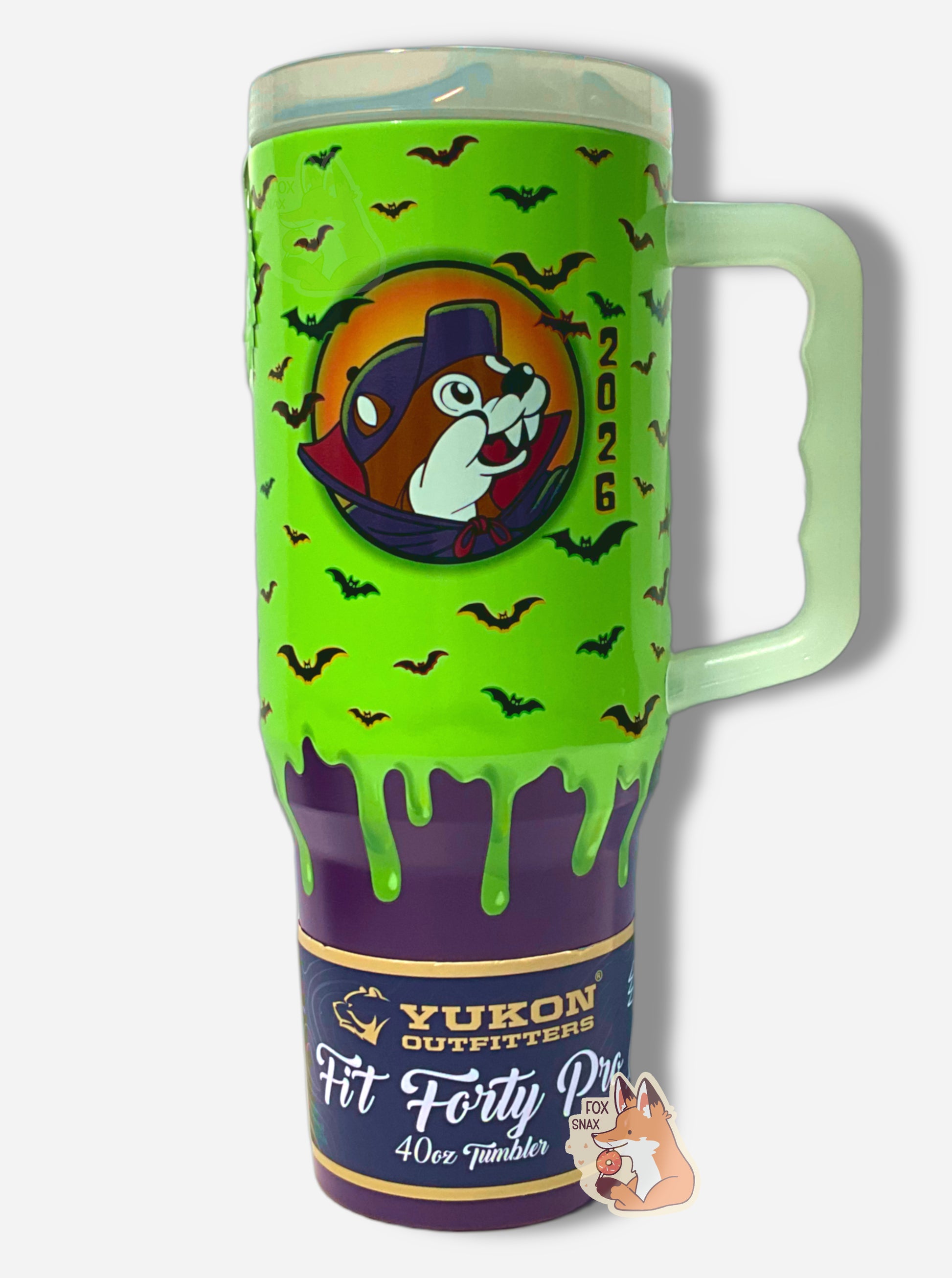 A picture of a tall, green and purple sorta skinny tumbler, with a giant picture of Buc-ee in the middle, wearing a red/blue vampire cowl. The background behind him appears to be a orange/yellow full moon, and he has, interestingly, two fangs instead of the usual beaver overbite. The background is green slime 'dripping' down the tumbler, with black bats against that background.  The bottom fades to solid purple. The tumbler is paint covering stainless steel. The handle and top are glow in the dark plastic. 
