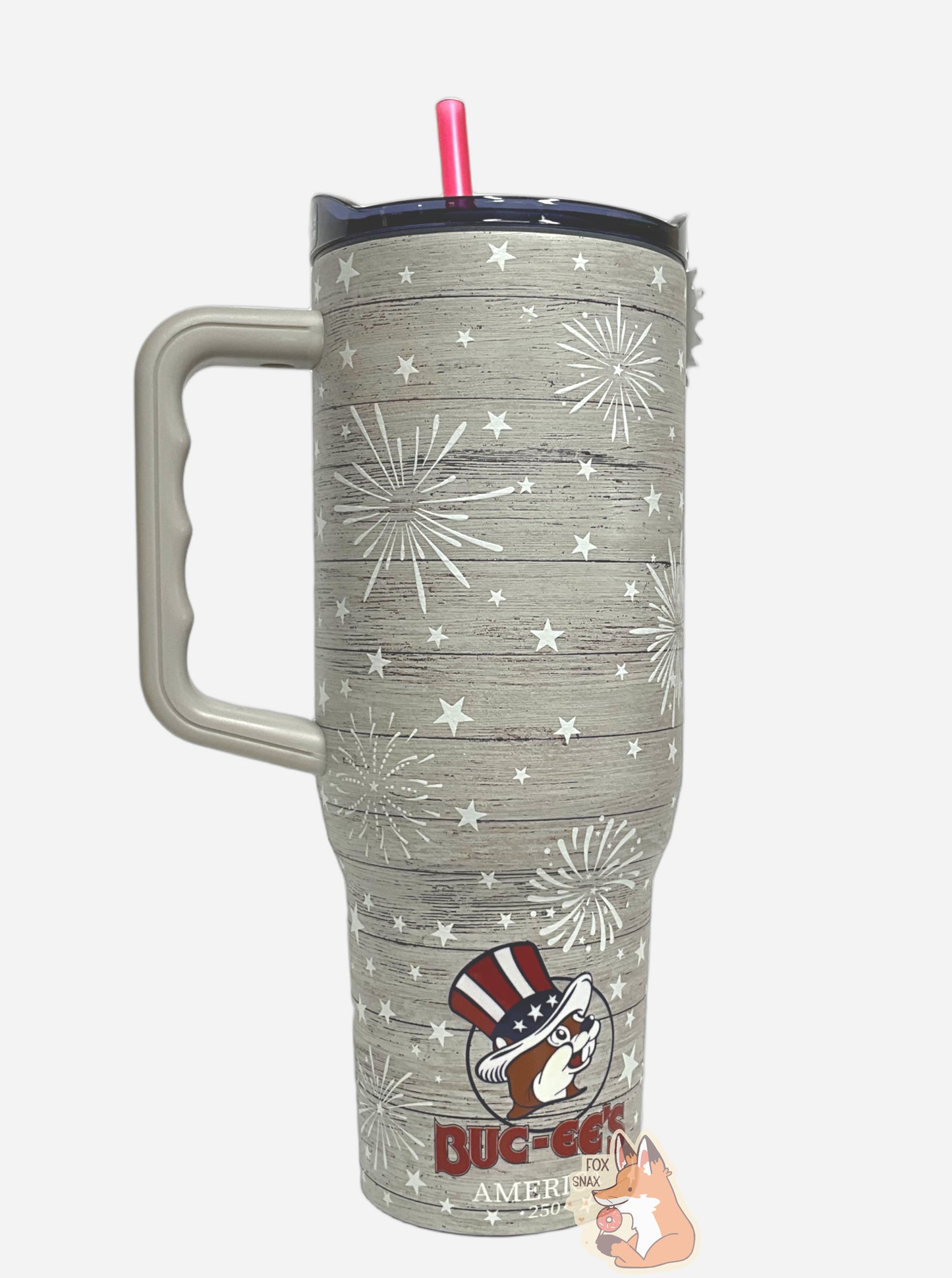 A picture of a tall, grey "woodgrain", sorta skinny tumbler, with a small picture Buc-ee The Beaver on it wearing a red, white, and blue Uncle Sam hat.  The surface is slightly textured, grey,  covered with white stars and white exploding fireworks.  Underneath the logo, it reads AMERICA then 250.  It is grey paint covering stainless steel. The handle (grey), top (blue) and straw (red) are plastic; a Yukon Outfitters Fit Forty 40 oz Tumbler.  