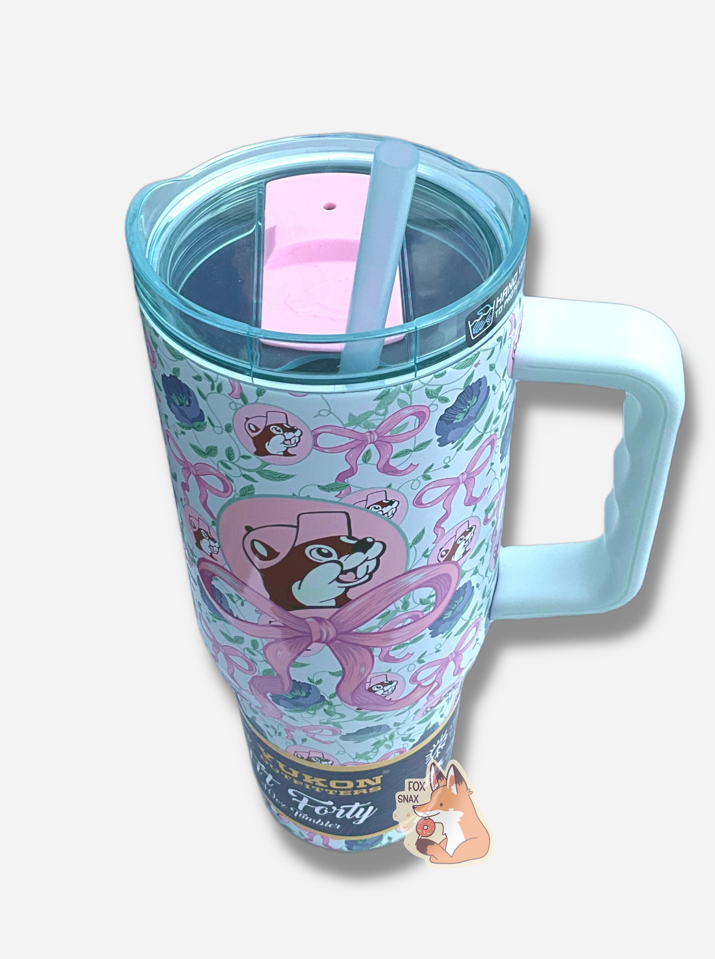 A picture of a tall, light blue, sorta skinny tumbler, with a big picture of Buc-ee The Beaver on it.  Buc-ee's hat, and the circle behind him, is in light pink, and is framed by a large light pink bow.  The surface is dotted with Buc-ee's logos, the pink bows, and dark blue flowers.  It is matte paint in covering stainless steel.  The handle, top, and straw are light blue (the top and straw are transparent) and plastic.  The top of the tumbler shows a slider for drinkin with two positions, in pink plastic.