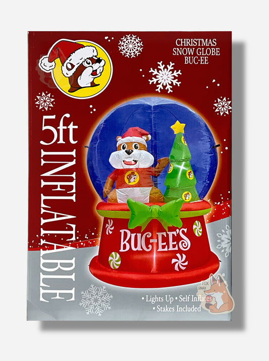 A large rectangular box, with a picture of a five foot, inflatable snow globe with Buc-ee The Beaver in it, with his left paw raised up, and his right down at his side.  He is wearing a red shirt, with a Buc-ee's logo on it.  The inflatable is wearing a large Santa hat.  Next to Buc-ee is a green Christmas tree decorated with a star.The box reads: 5 ft Inflatiable.  Christmas Snow Globe Buc-ee.  Lights up.  Self Inflates. Stakes Included.  The background is in red  and has various snowflakes dotting it.