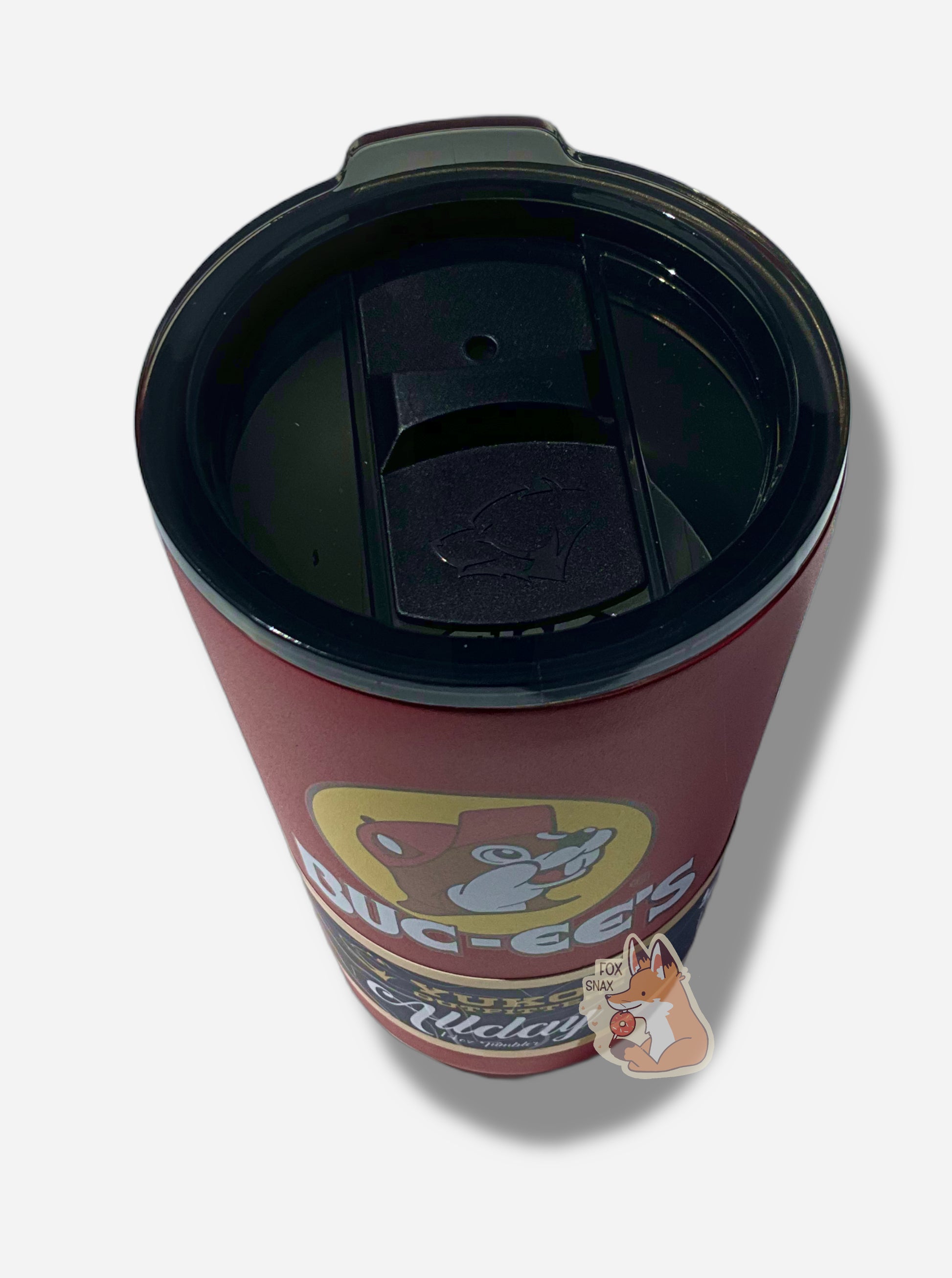 A three-quarters perspective picture of the top of a small 14oz tumbler.  The surface of the cup is red paint over metal.  The top of the cup features a clear plastiic lid.  The top of the lid is removed; it's black plastic with a small sipping area on the exterior, near a red teardrop-shaped slider with the Yukon Outfitters logo (a grumpy bear) on top. On the top, a black three-position slider can be seen.