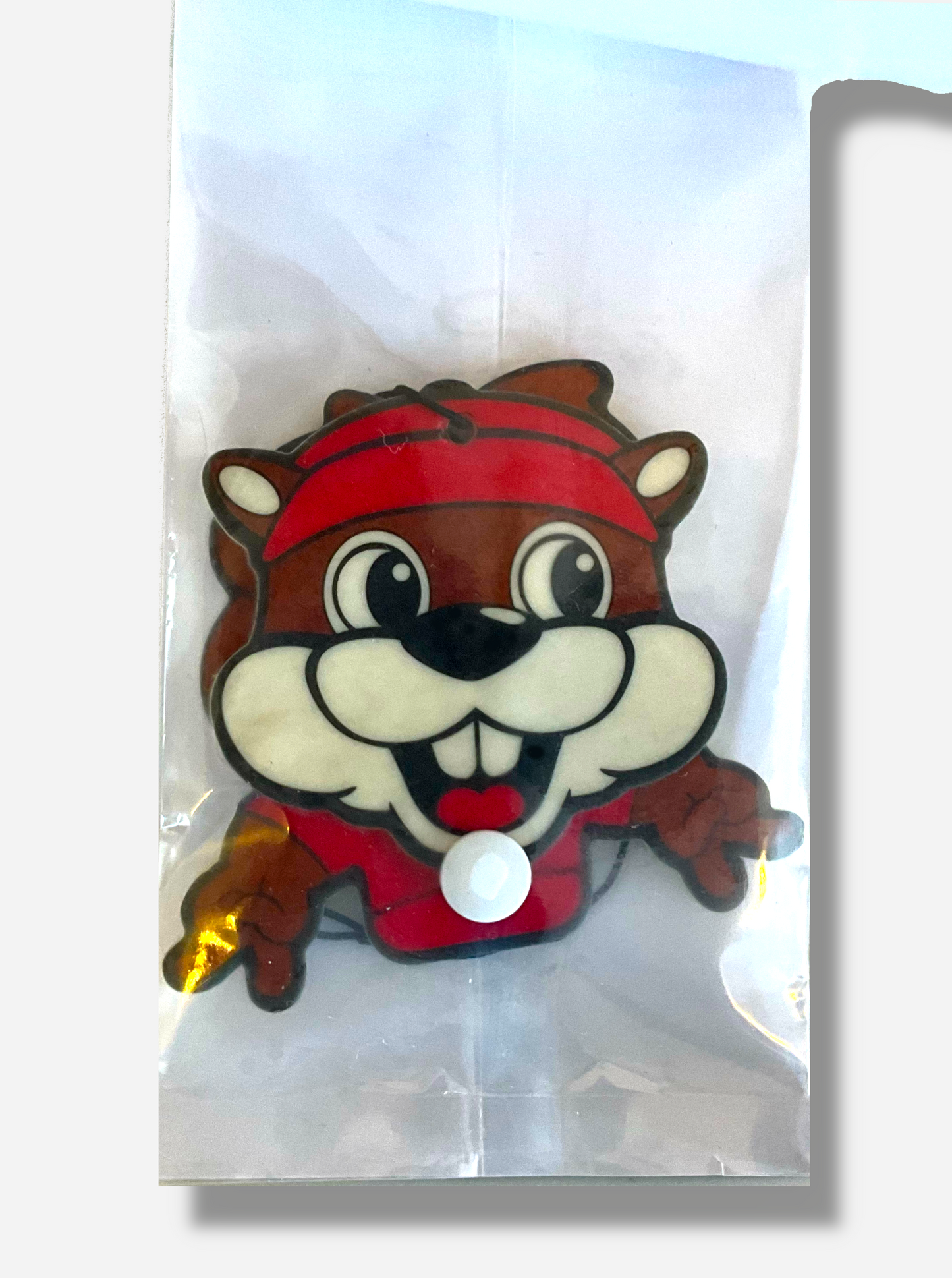 A picture of the inside of a Buc-ee's Wiggler Air Fresher.  Buc-ee is smiling, showing his buck teeth and tongue, and his large eyes are looking to the right.  Each of his hands are holding up the peace sign.