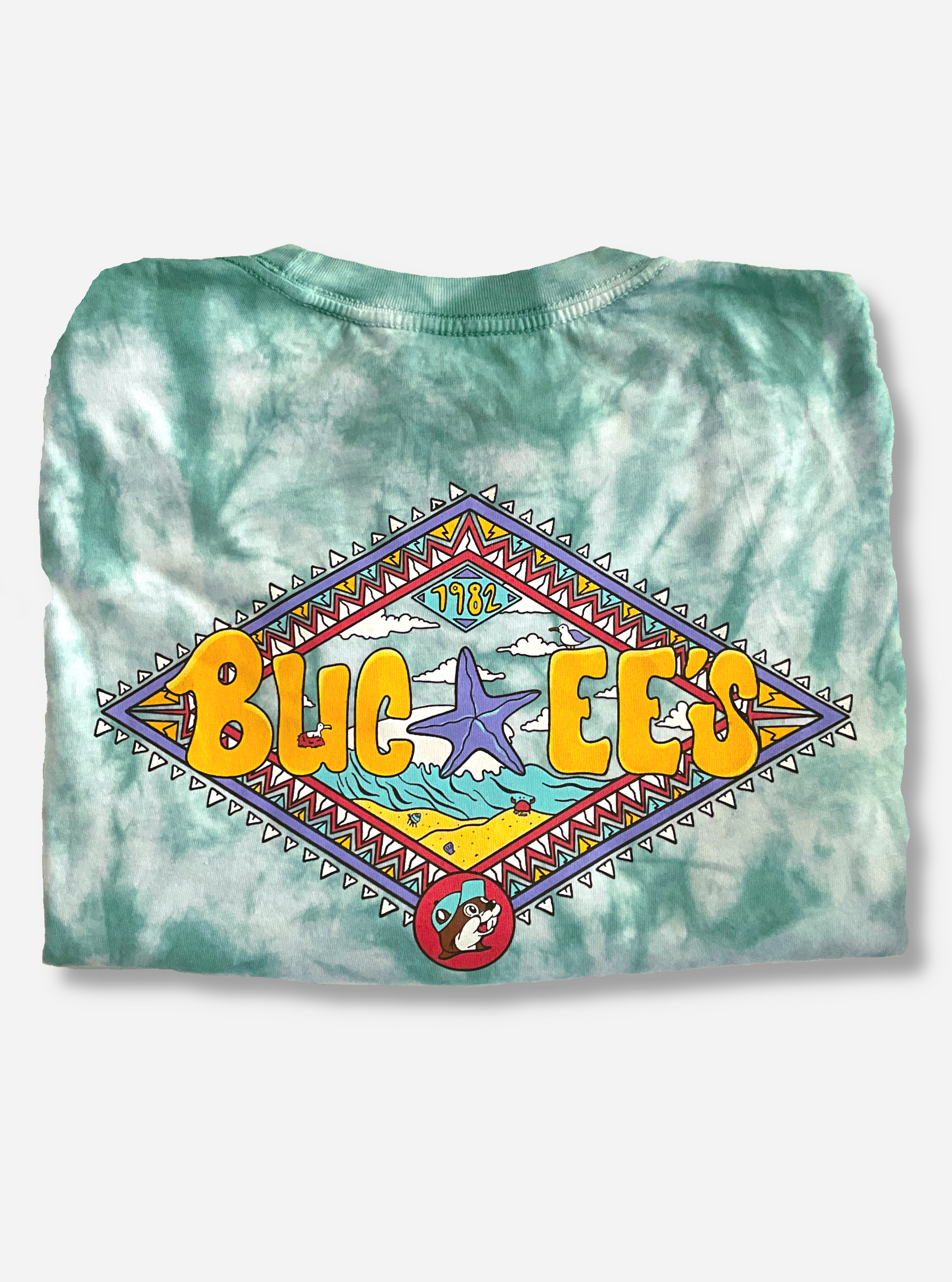 The back of a Buc-ee's Aztec t-shirt.  The background on the shirt is a blue/green tie dye color, against a white background.  The center of the shirt is dominated by a large diamond shape with Aztec coloring of purple, light blue, yellow, red, and white triangles bordering it.  The center of the diamond states BUC-EE's in yellow curvy letters, with a large purple starfish in the middle.  The background behind the starfish is that of a beach with cresting wave.  The Buc-ee's beaver logo is on the bottom.