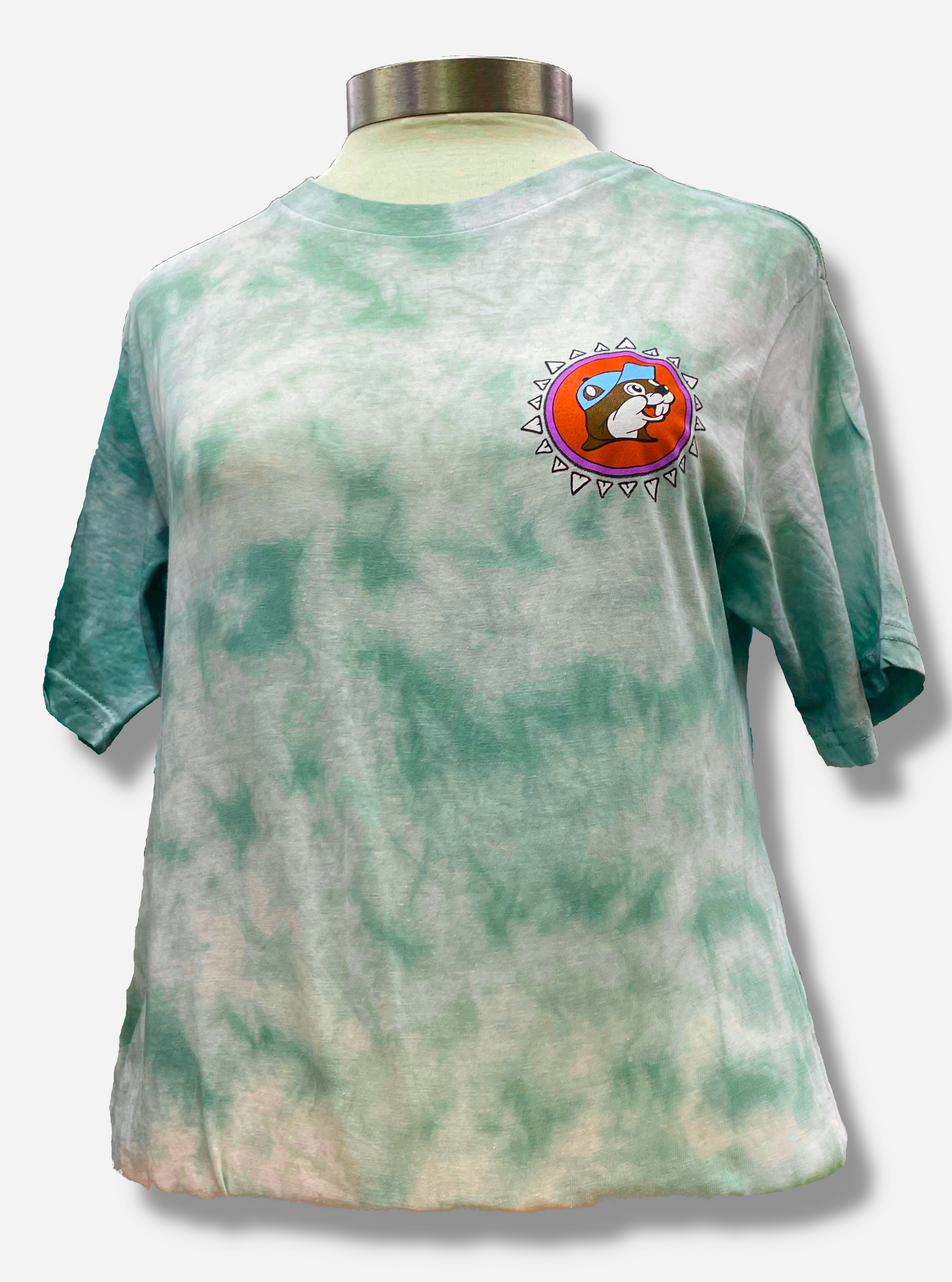 The front of a Buc-ee's Aztec t-shirt on a manikin torso.  The background on the shirt is a blue/green tie dye color, against a white background.  On the front right of the shirt is the Buc-ee's logo, but the background is pink, not yellow.  Buc-ee's hat is a light blue, not red.  Finally, the logo is surrounded by a series of white triangles to give it an Aztec-like theme.