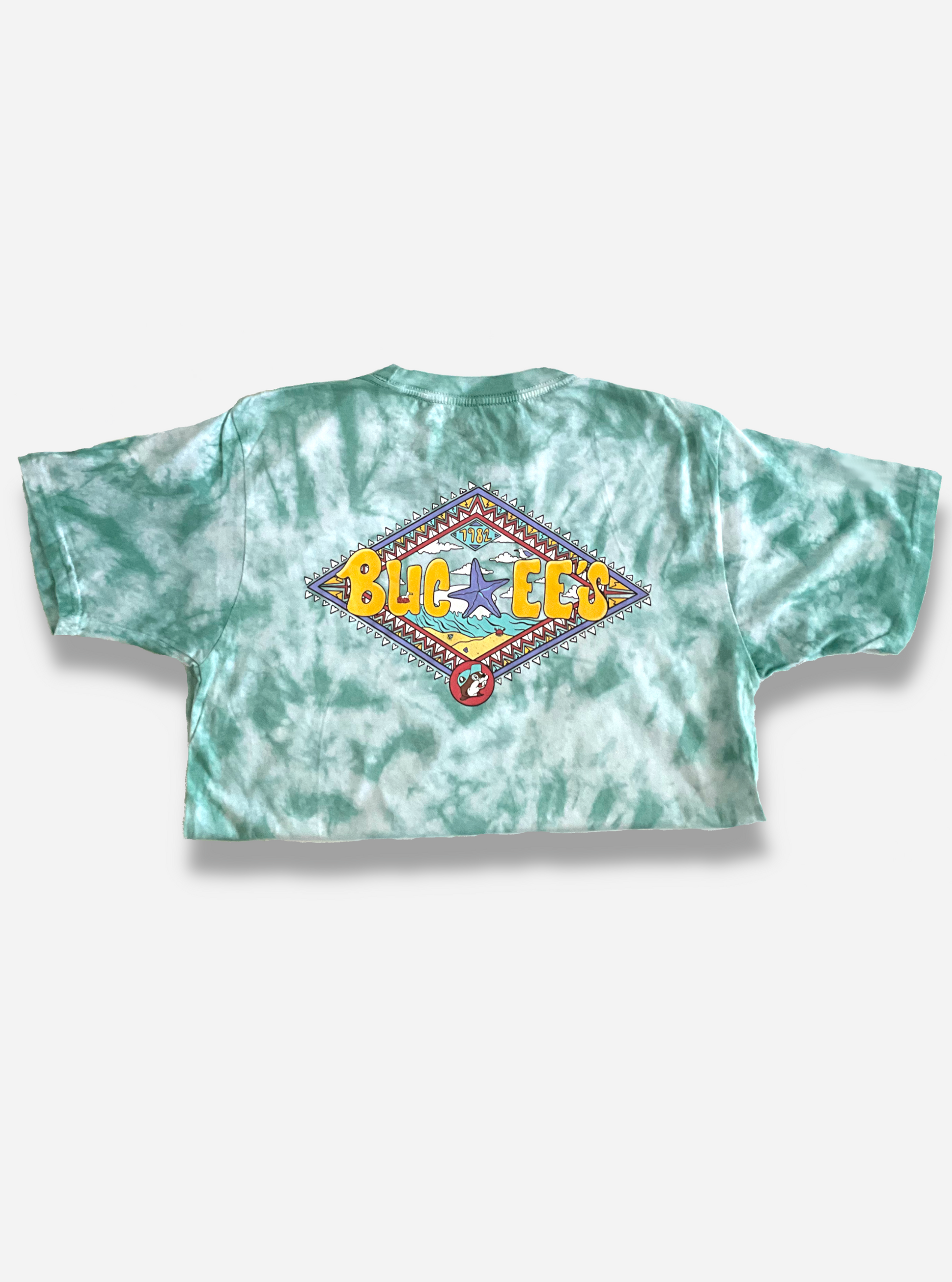 The back of a Buc-ee's Aztec t-shirt.  The background on the shirt is a blue/green tie dye color, against a white background.  The center of the shirt is dominated by a large diamond shape with Aztec coloring of purple, light blue, yellow, red, and white triangles bordering it.  The center of the diamond states BUC-EE's in yellow curvy letters, with a large purple starfish in the middle.  The background behind the starfish is that of a beach with cresting wave.  The Buc-ee's beaver logo is on the bottom.