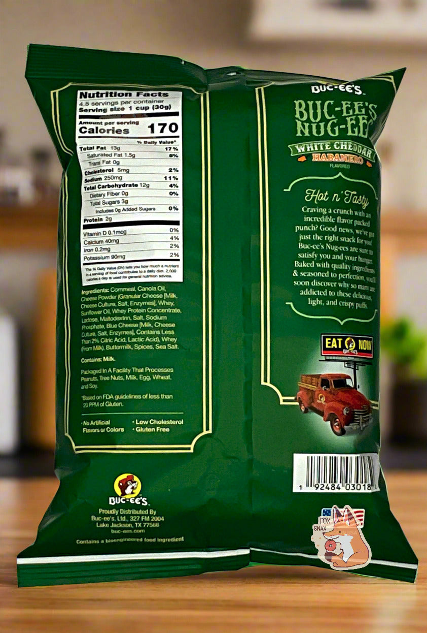 A picture of the back of a opaque, dark green and light green bag of Buc-ee's Nug-ees White Cheddar Habanero Nug-ee's.  A panel on the back reads Hot N' Tasty, then Craving a crunch with an incredible flavor packed punch?  Good news, we've got just the right snack for you!  Buc-ee's Nug-ee's are sure to satisfy you and your hunger.  Baked with quality ingredients & seasoned to perfection, you'll soon discover why so many are addicted to these delicious, light, and crispy puffs.  Background is a kitchen.