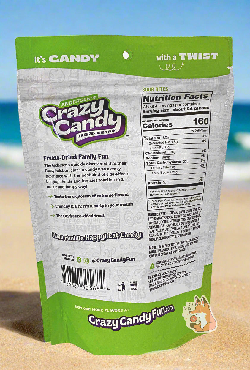 The back of a large bag of Andersen's Crazy Candy Sour Bites.  The bag reads: Freeze Dried Family Fun.  The Andersens quickly discovered that their funky twist on classic candy was a crazy experience with the best kind of side effect: bringing friends and families together in a unique and happy way!  The bag is sitting on beach sand, with ocean waves crashing against the sand in the background against a blue sky.