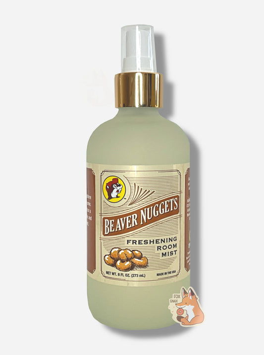 Front of a spray bottle of Buc-ee's Beaver Nuggets Freshening Room Mist on a white background.  The bottle is frosted glass with a white sprayer and gold label, and has the Buc-ee's logo in the top left.  The rest of the label has a series of brown lines, and reads BEAVER NUGGETS, then FRESHENING ROOM MIST, then NET WT 8 FL OZ, then MADE IN THE USA.