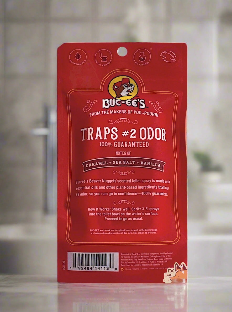 The back of a red package of Buc-ee's toilet spray on a white background.  The label reads BUC-EE'S, then FROM THE MAKERS OF POO~POURRI, then TRAPS #2 ODOR, 100% GUARANTEED, then NOTES OF CARAMEL & SEA SALT & VANILLA.  The background is of a marble bathroom.
