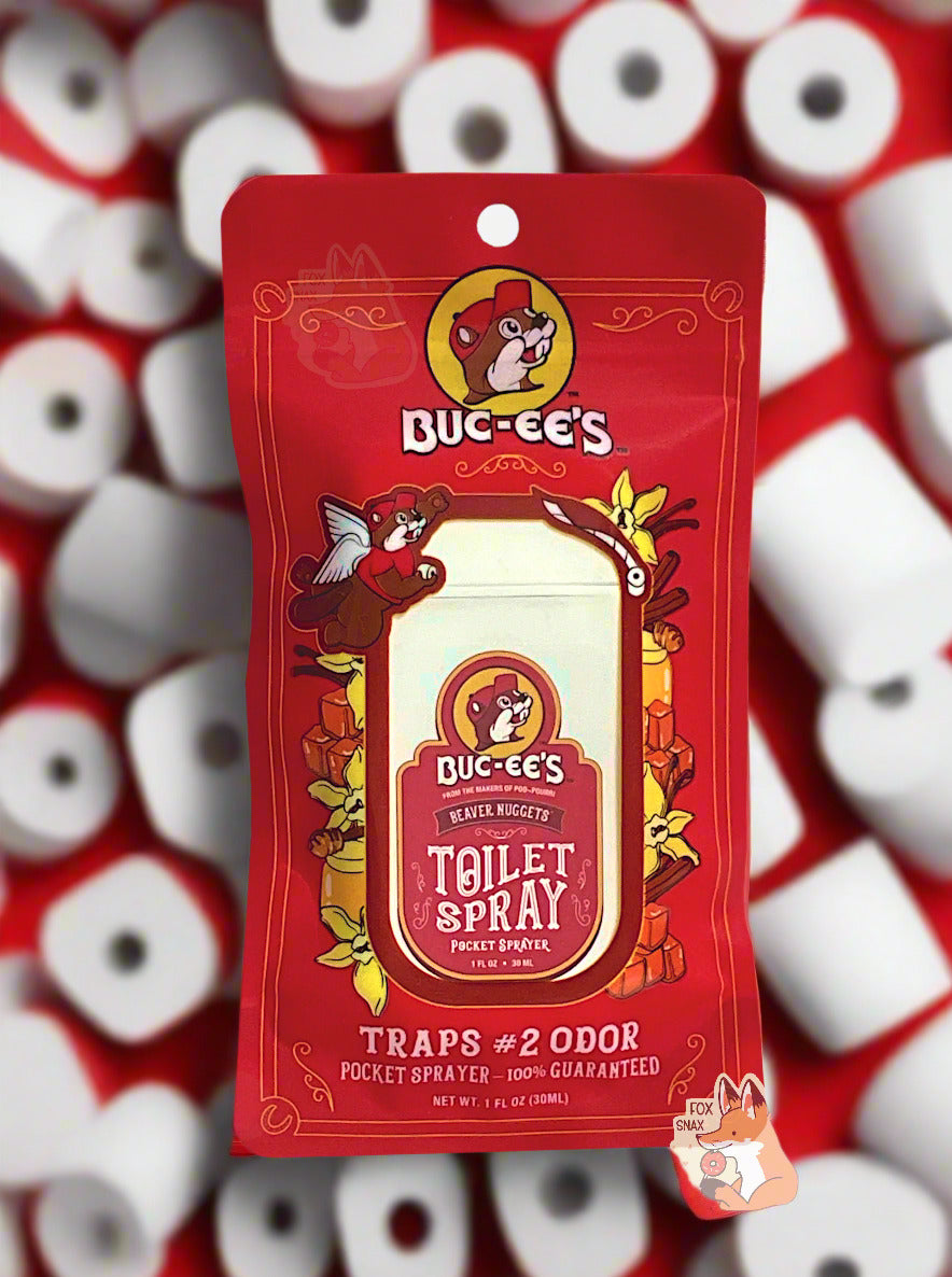 Red package of Buc-ee's toilet spray on a white background.  The label, amusingly, in the top left, has Buc-ee with a pair of angel wings, holding a roll of toilet paper in one paw, and in the other, outraised, throwing a roll of toilet paper.  The label reads: BUC-EE'S, FROM THE MAKERS OF POO~POURRI, BEAVER NUGGETS POCKET TOILET SPRAYER, then TRAPS #2 ODOR, then 1 FL OZ.  The background is littered with tens of rolls of white toilet paper.