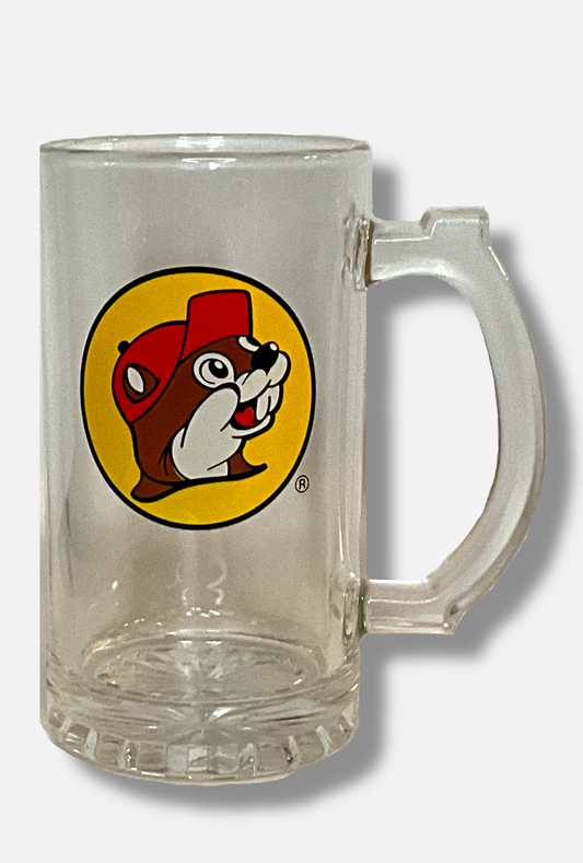 A picture of the front of clear beer mug. The glass is clear. In the middle of the front is the Buc-ee's logo, which appears inside a yellow circle; it is a cheerful beaver wearing a red ballcap, against a yellow circle background.  The handle of the beer mug is also clear, and slightly blocky.  A ridged thumb area on the top can be seen.  