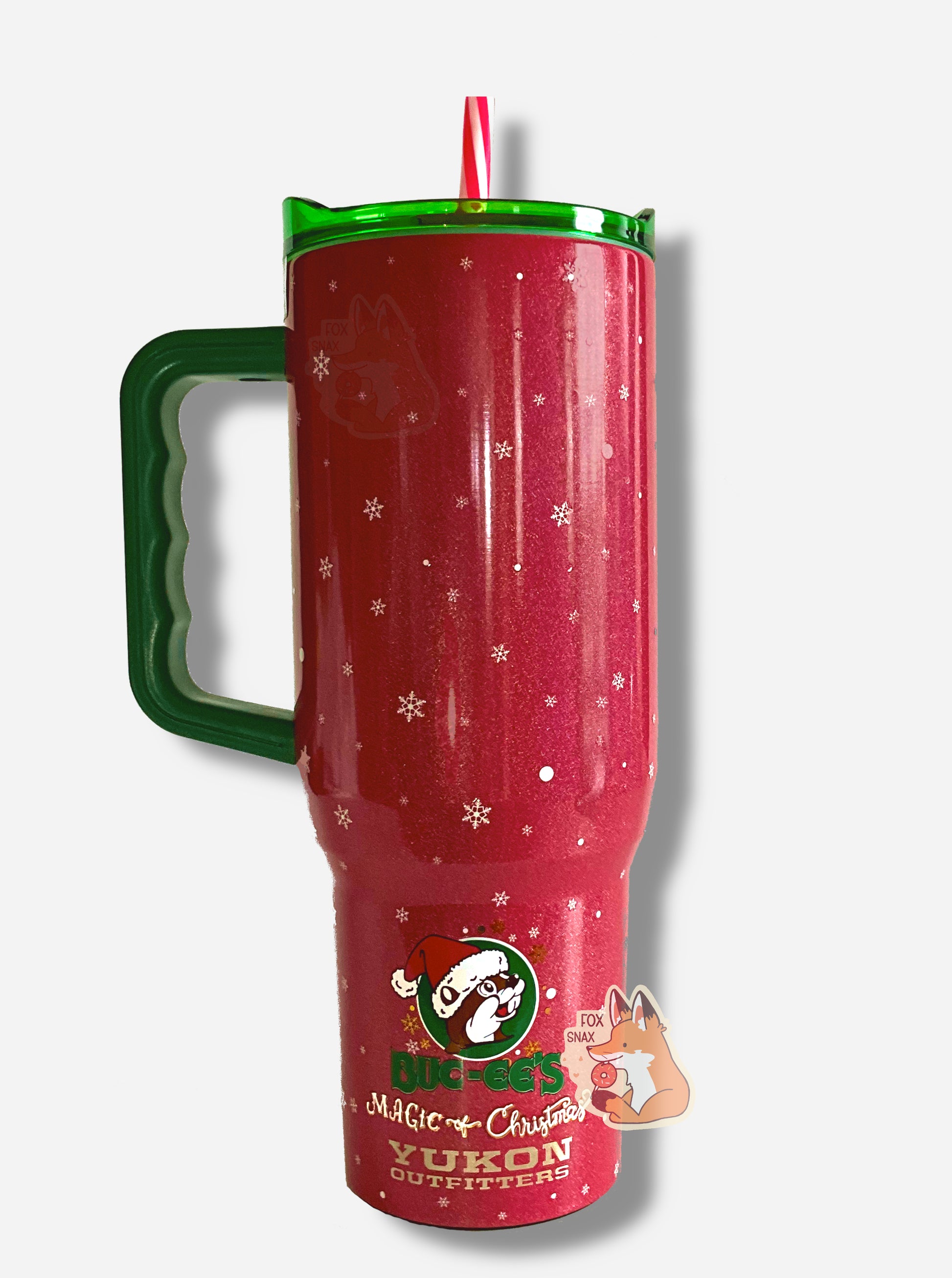 A picture of the back of a tall, maroon and red, skinny tumbler, with Believe In the Magic of Christmas written in white text. The tumbler is paint covering stainless steel.  The handle, top, and candy-cane colored straw are plastic.  The bottom reads: "BUC-EE'S Magic Of Christmas", in white and green text, then, underneath that "YUKON OUTFITTERS" in gold text