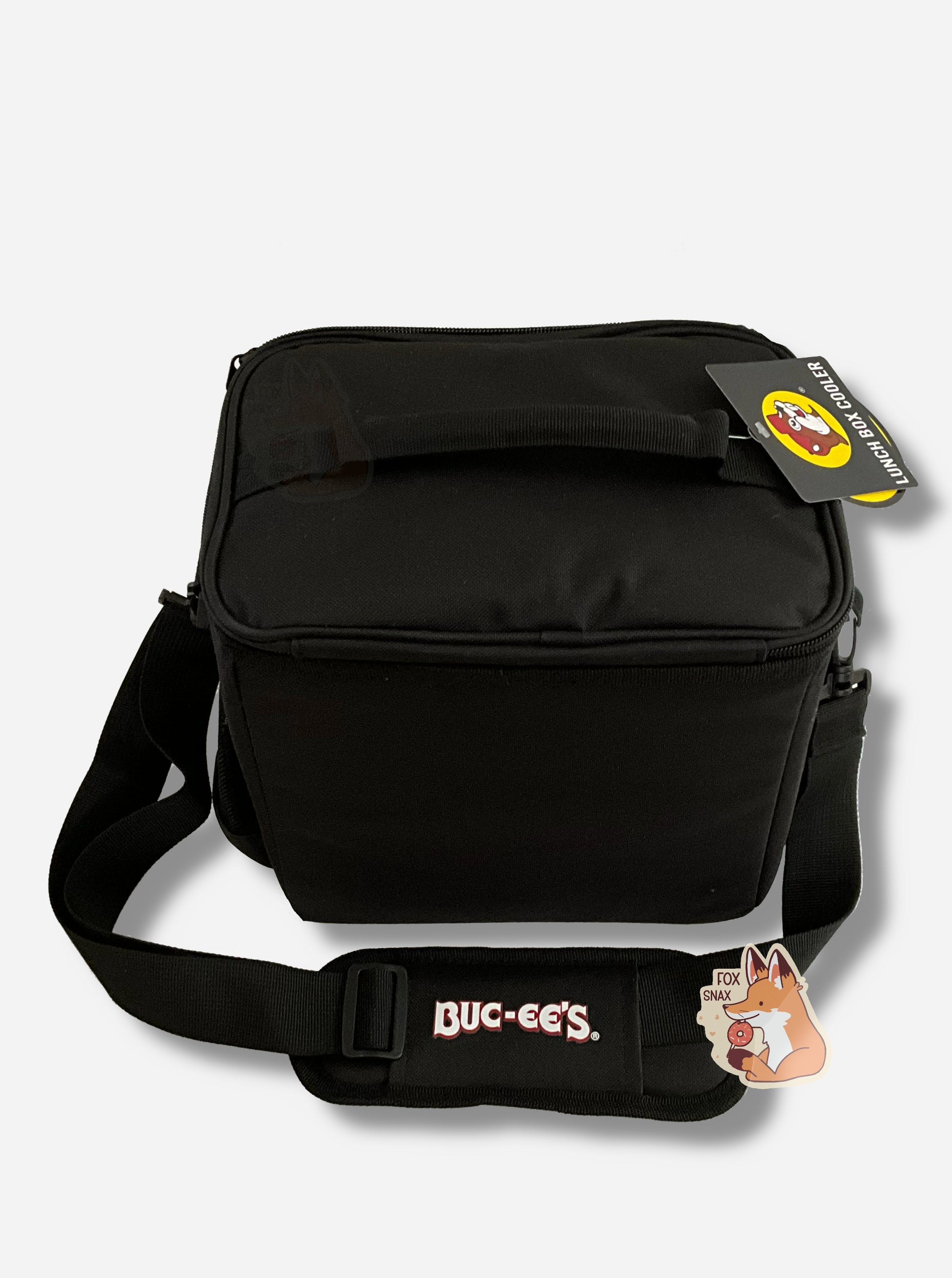 A picture of a the back of a lunch box cooler.  The outer surface is made of black polyester, and has large black strap on it that reads BUC-EE'S.  The top of the lunch box has a black fabric handle.