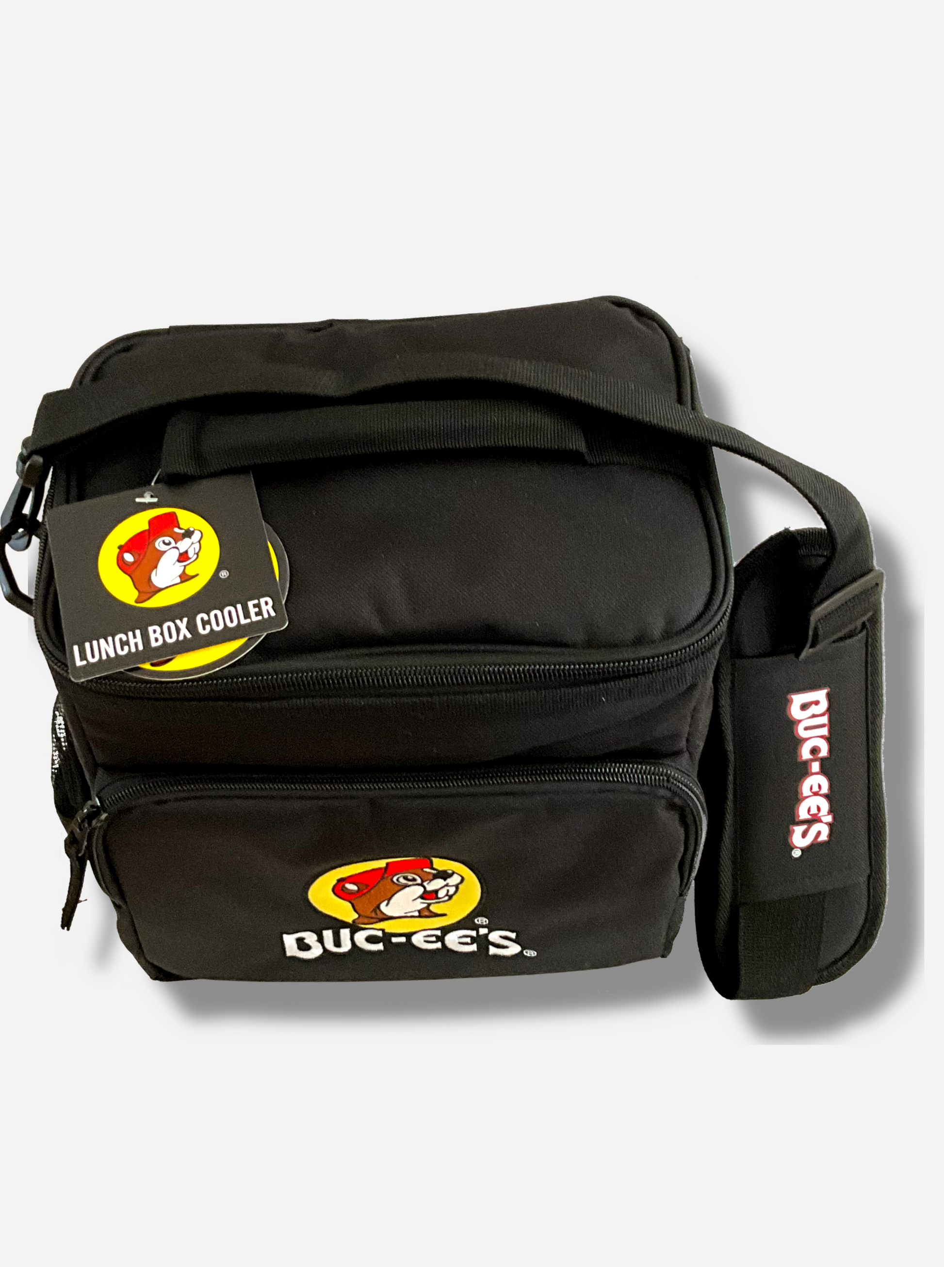 A picture of a three-quarters view of the front of a large lunch box cooler.  The outer surface is made of black polyester, and has a large black strap on it that reads BUC-EE'S.  The front of the lunch box has a zip pouch, with the Buc-ee's logo on it: a grinning beaver wearing a red hat against the background of a yellow circle.  The sides of the tote has mesh pouches, the top sealed by a zipper.