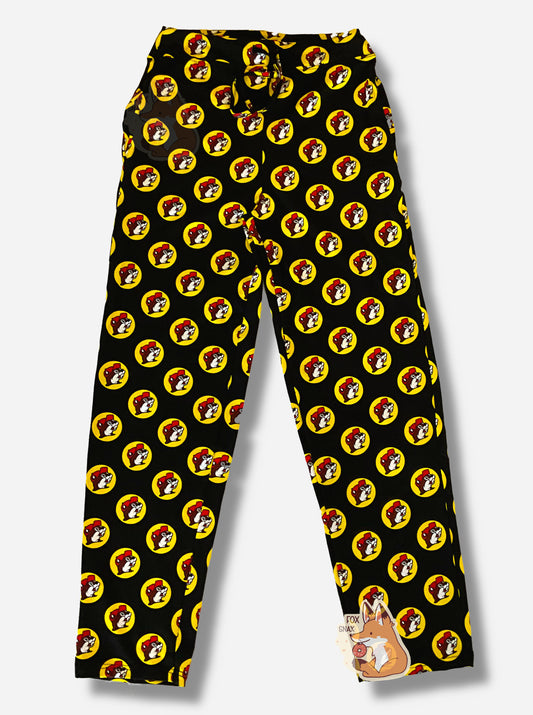 A picture of a pair of black pants.  The pants are covered in Buc-ee's logos: a grinning beaver wearing a red ballcap, backlit by a yellow circle.  A black drawstring can be seen at the waist of the pants.