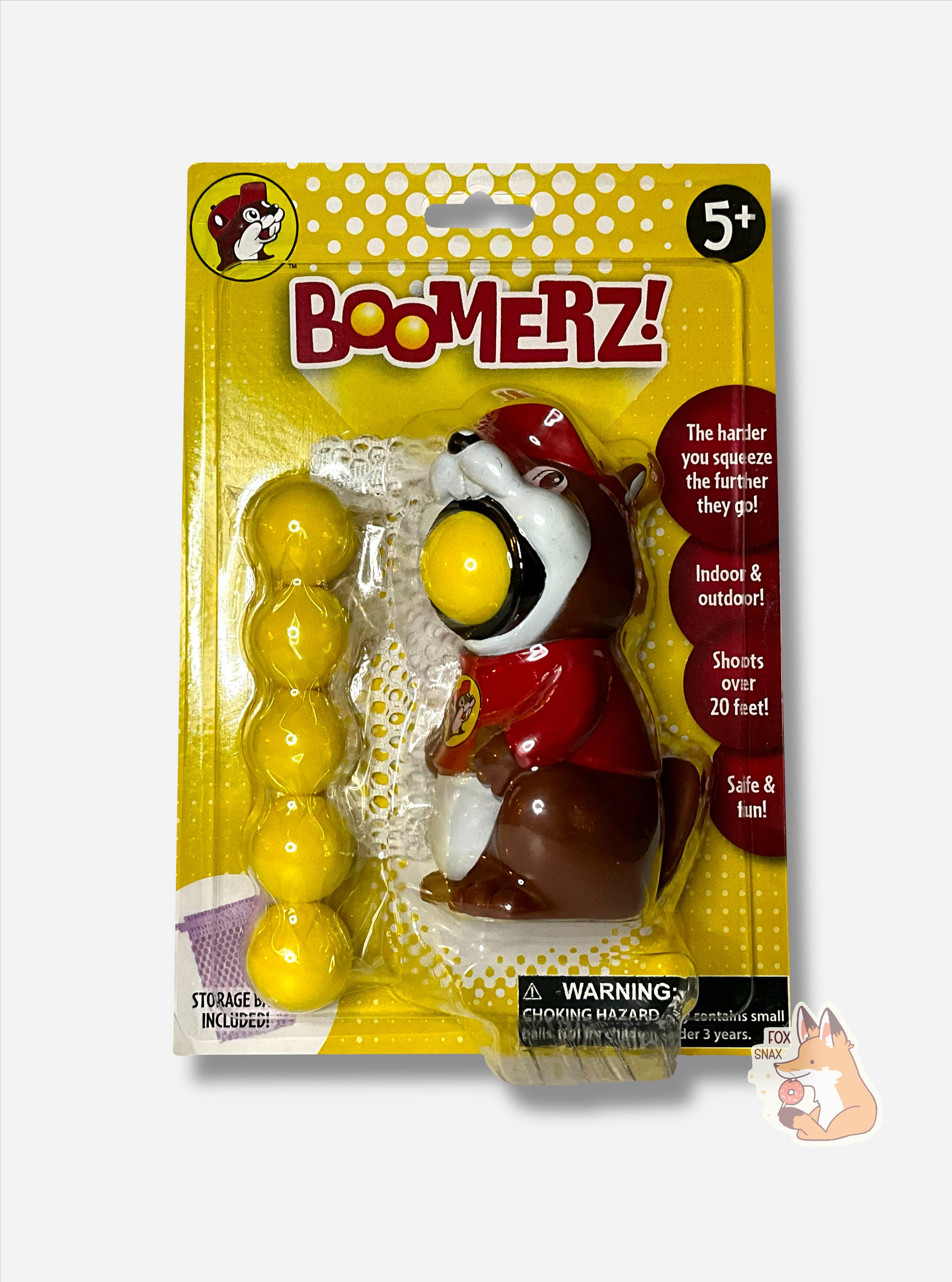 A package of Buc-ee's Boomerz!  The package is in yellow, and shows a Buc-ee the Beaver toy with a large yellow ball in his mouth.  Five more balls can be seen to the left in the package.  The package reads: THE HARDER YOU SQUEEZE THE FURTHER THEY GO! then INDOOR & OUTDOOR then SHOOTS OVER 20 FEET!, then SAFE & FUN!  A black circle in the top right reads 5+.  A small white mesh bag can be seen behind the Buc-ee figure.