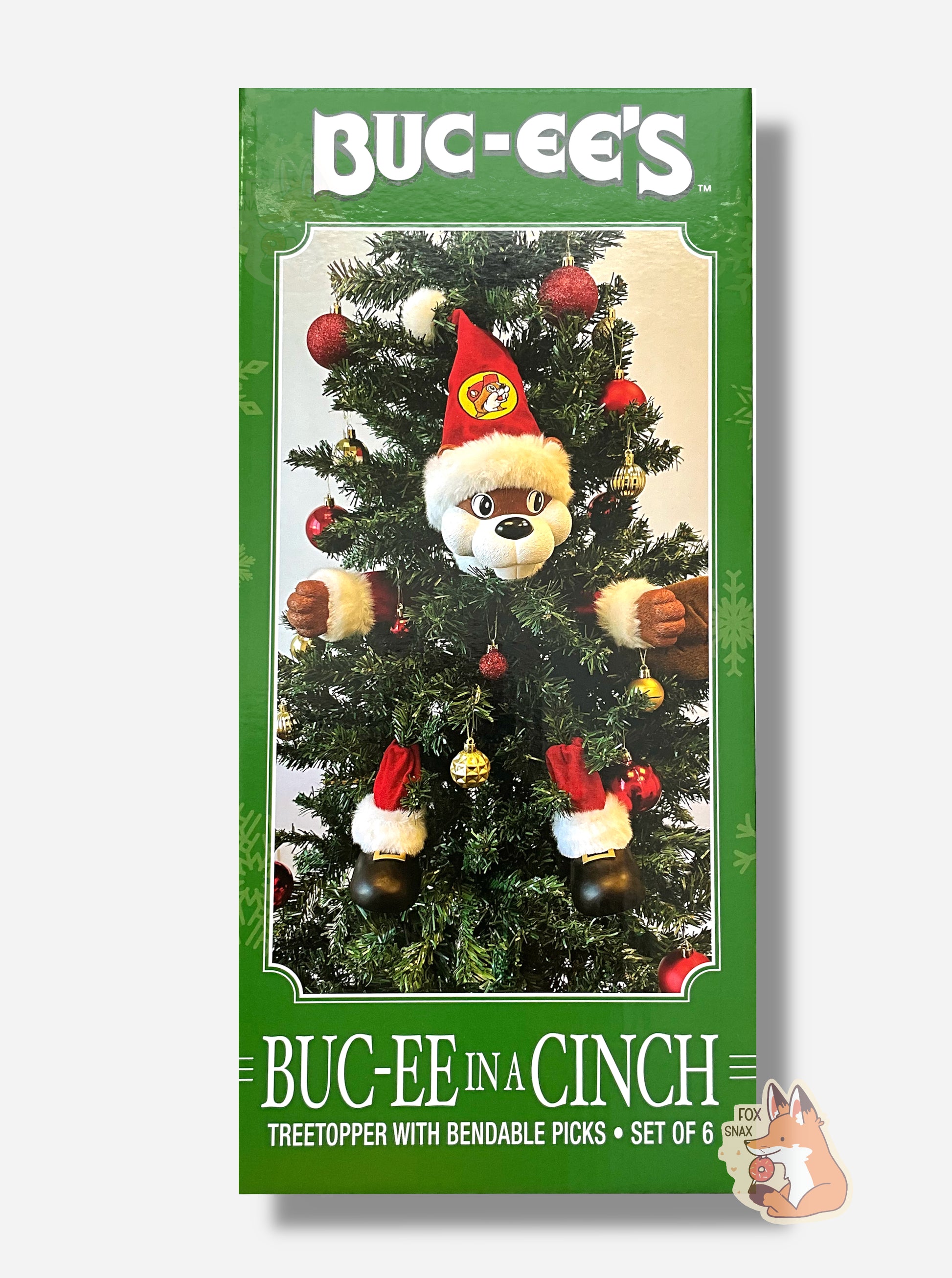 A picture of the side of a green box that reads BUC-EE'S BUC-EE IN A CINCH, Treetopper with bendable picks, set of 6, in white text.  In the center of the box is a Christmas tree, decorated with ornaments.  Going clockwise from top middle are: Buc-ee The Beaver's head, wearing a red pointed cap with a Buc-ee's logo, Buc-ee's left hand, Buc-ee's tail, Buc-ee's left leg, Buc-ee's right leg, then Buc-ee's right hand.  Buc-ee's arms and legs are suited with a red Santa-like outfit; his shoes are black.