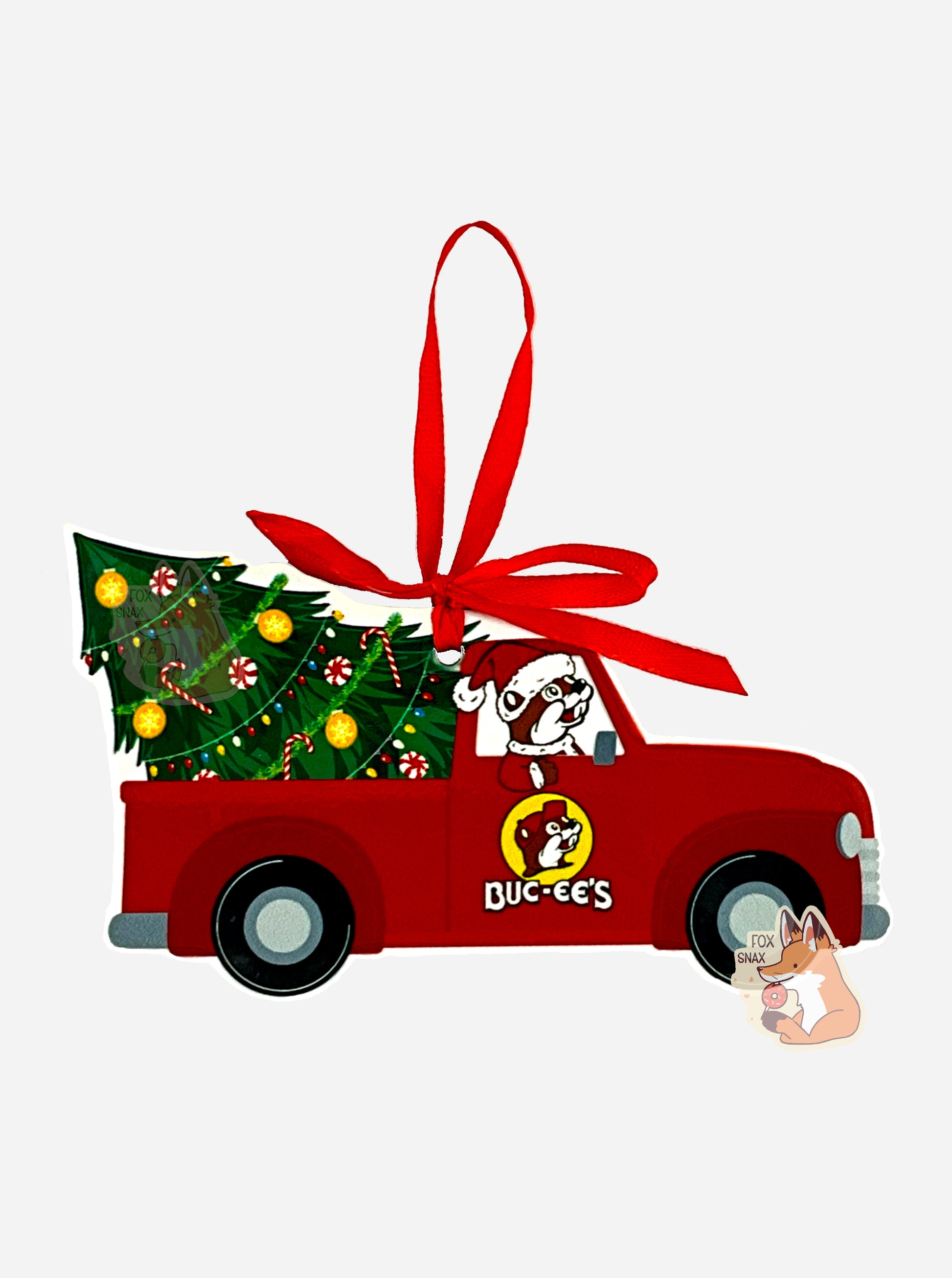 A picture of the front of a ceramic, mostly truck-shaped ornament, with a red ribbon at the top to hang it on a tree.  The ornament has a red old-style pickup truck, with Buc-ee The Beaver driving, with his paw hanging out the window.  Buc-ee is wearing a Santa hat.  The pickup truck's bed has a well decorated Christmas tree sitting in the bed, partially tipped over.  Candy canes, ornaments, colorful lights, and green garland decorate the tree.  The ornament is laid against a pure white background.