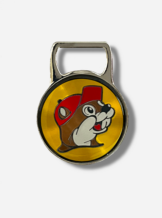 A picture of the front of a metallic bottle opener.  The top of the opener is a grey metal and shaped to open bottles.  The bottom of the opener is a circle, which contains the Buc-ee's logo - a cheerful beaver wearing a red ball cap, in front of a yellow circle logo.