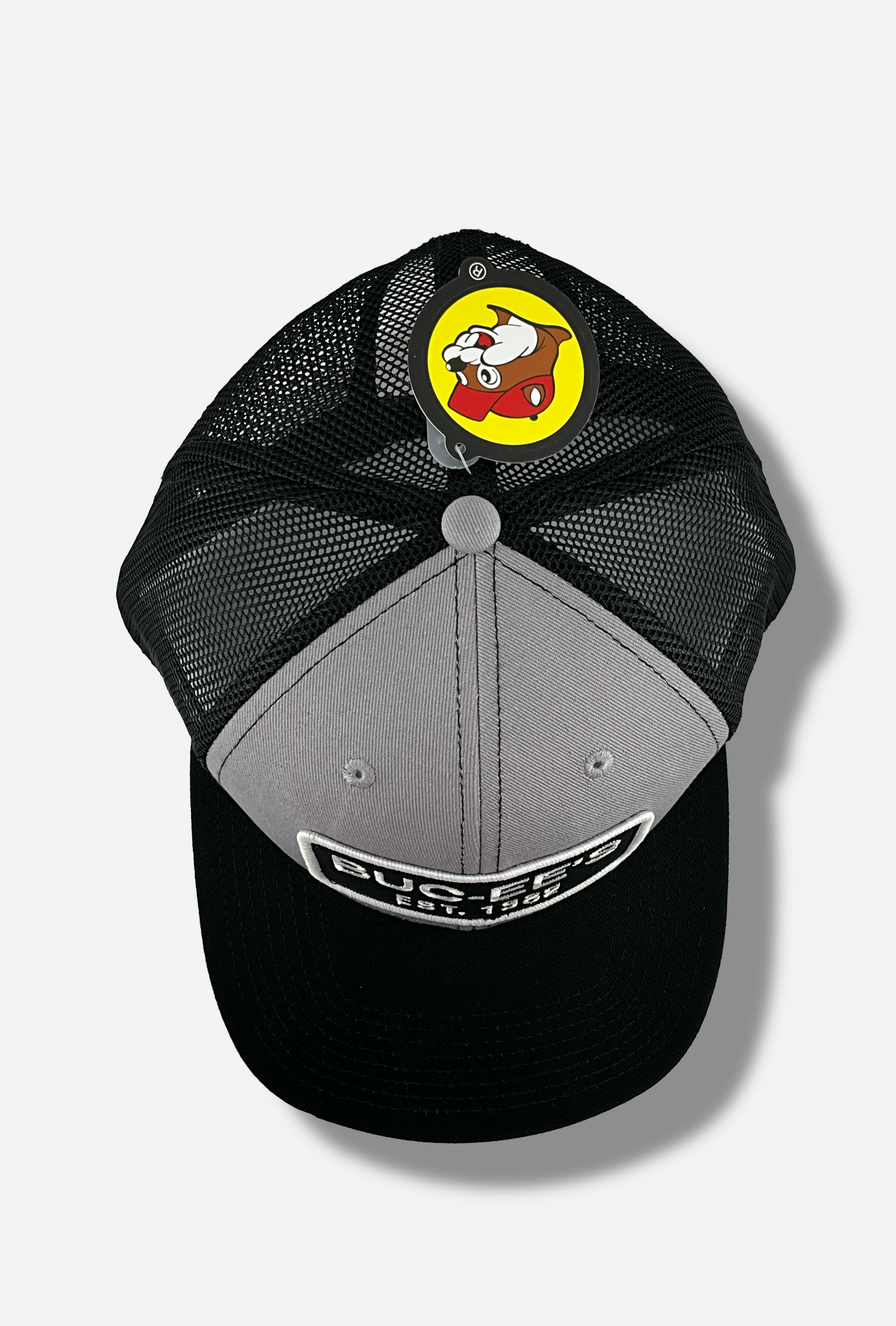 A picture of the top of a grey and black ball cap.   The front of the cap is grey, and has a large white and black rectangular patch that reads BUC-EE'S, and underneath that, EST. 1982.  The brim of the cap is black.  The back and sides of the cap are a black plastic mesh.