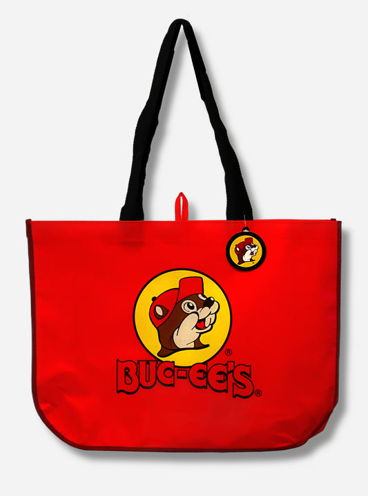 A picture of a large red plastic shopping bag with the Buc-ee The Beaver logo on it.  The bag itself reads BUC-EES.  The strap on the bag is made of black cloth.