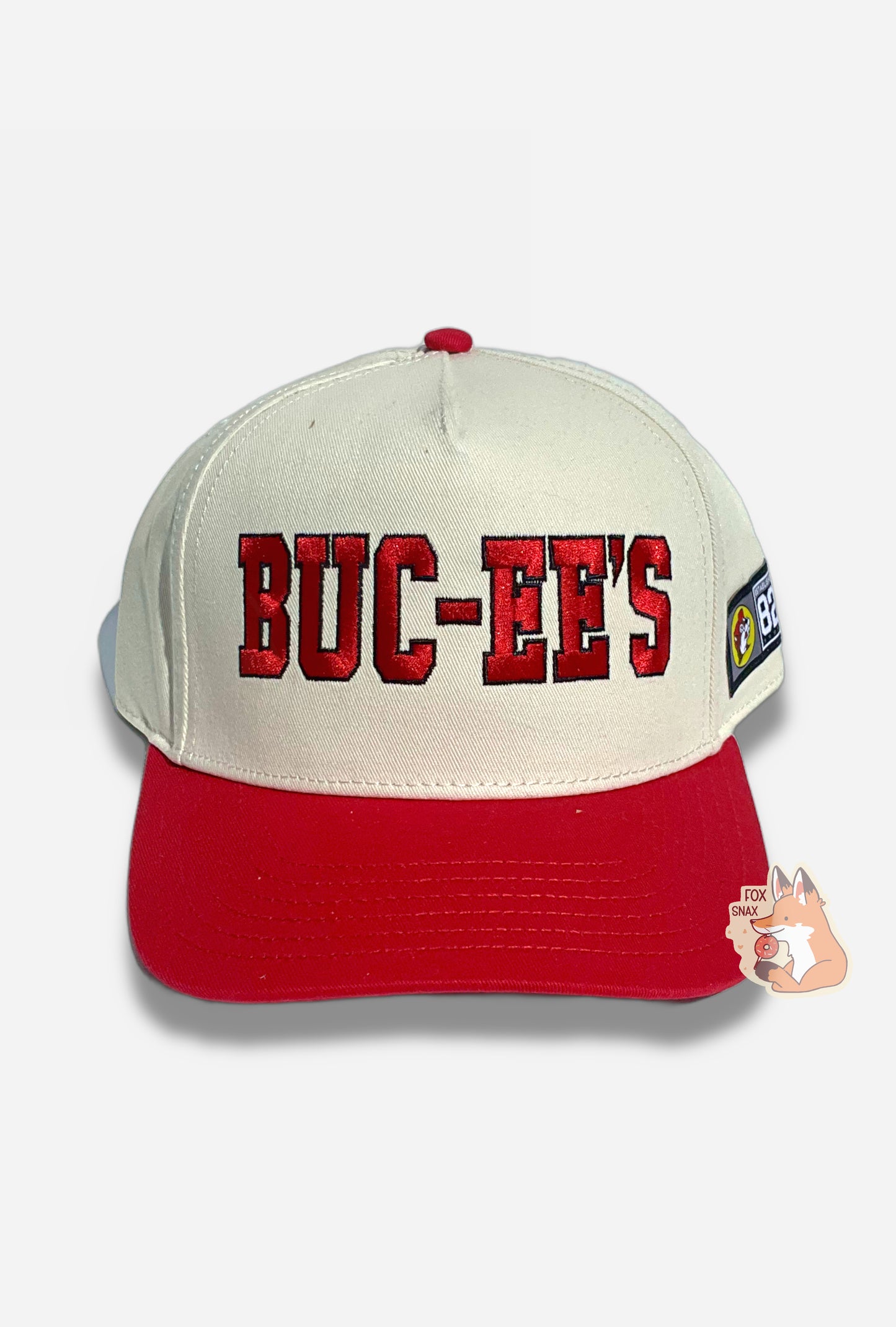 A picture of a red and white baseball cap.   The front of the cap is white and has large stitched letters that read BUC-EE'S in red, bordered in black thread.  The brim is red, and the button on top of the cap is also red.  The back and sides of the cap are a white cloth.