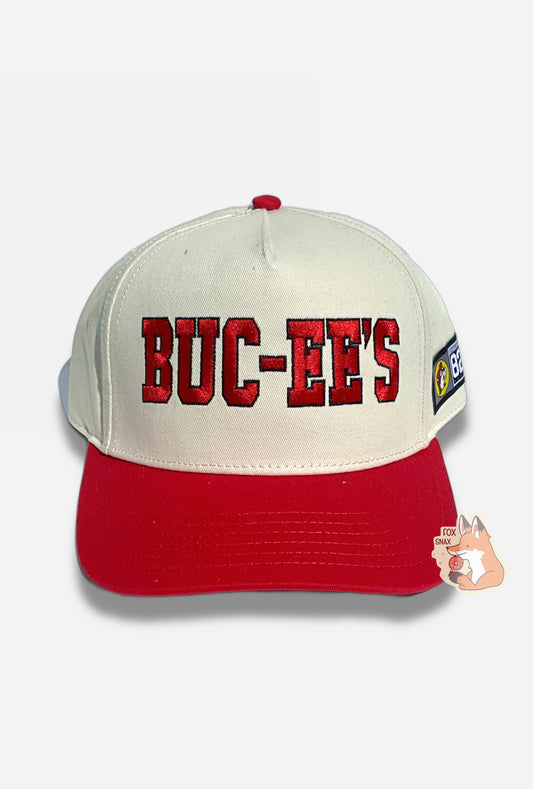 A picture of a red and white baseball cap.   The front of the cap is white and has large stitched letters that read BUC-EE'S in red, bordered in black thread.  The brim is red, and the button on top of the cap is also red.  The back and sides of the cap are a white cloth.