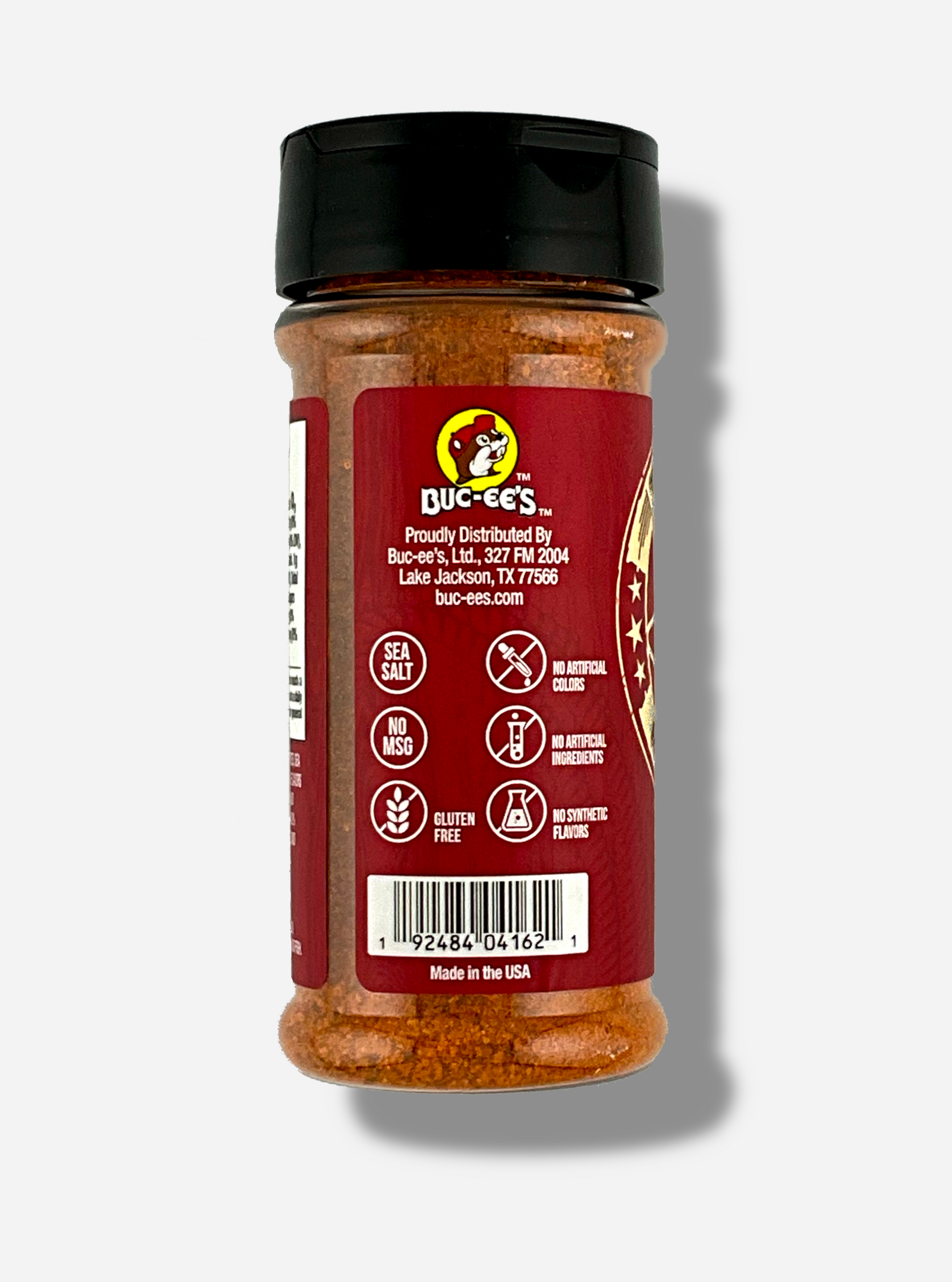 A picture of the side of a container of Texas Round Up BBQ Rub.  The container has a black plastic flip lid, and a clear plastic body.  The spices inside appear red/orange and black.  The red label reads SEA SALT, NO MSG, GLUTEN FREE, NO ARTIFICIAL COLORS, NO ARTIFICIAL INGREDIENTS, NO SYNTHETIC FLAVORS.  Beneath that, MADE IN THE USA