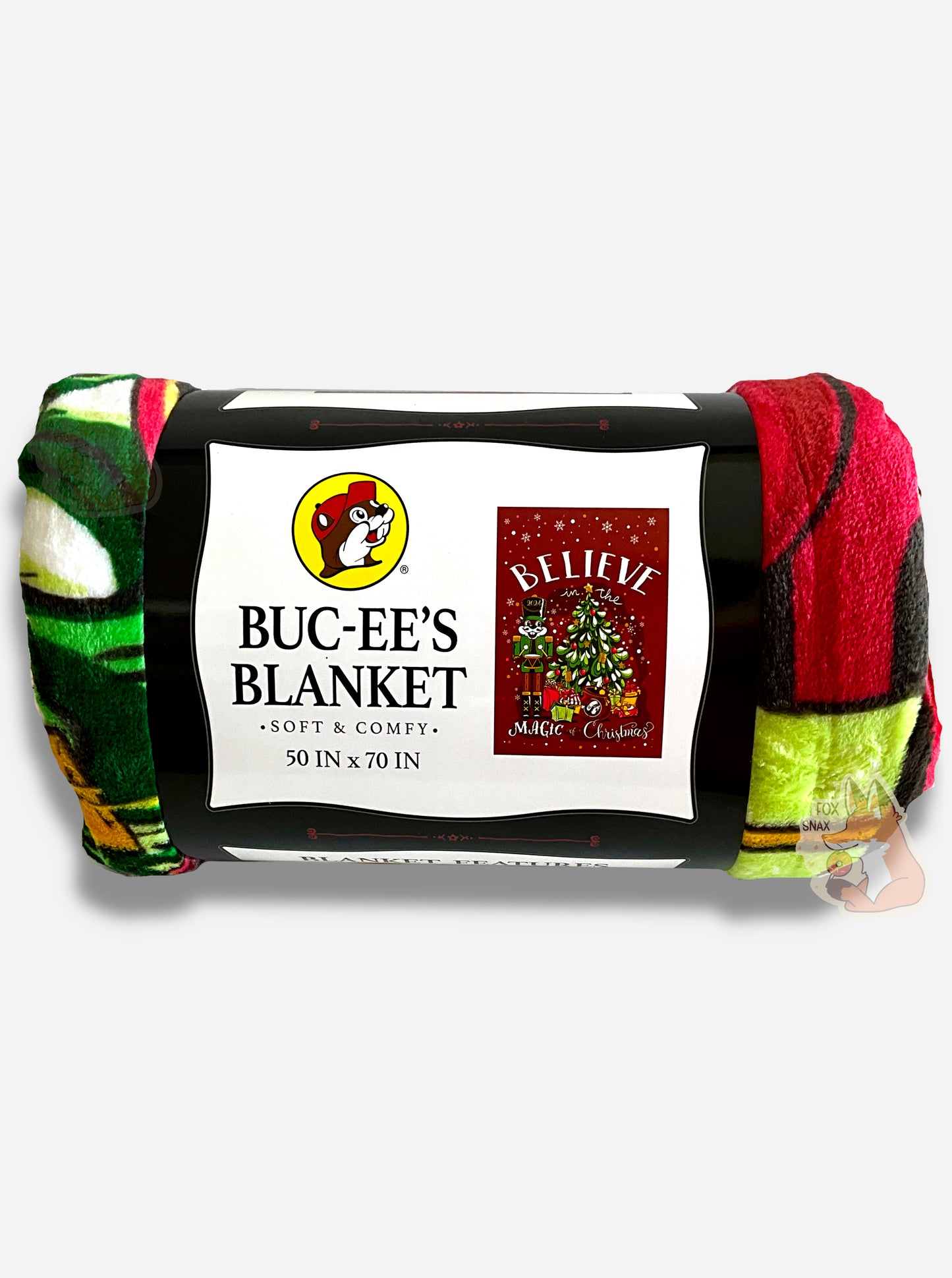 A picture of a soft red, black, green, and yellow blanket featuring Buc-ee the Beaver as a nutcracker, next to a Christmas tree.  The tree has many presents underneath, including a Buc-ee's logo.  The background is in red, framed by white snowflakes at the top, and reads BELIEVE IN THE MAGIC OF CHRISTMAS.  The label reads BUC-EE'S BLANKET *SOFT AND COMFY* 50 IN x 70 IN