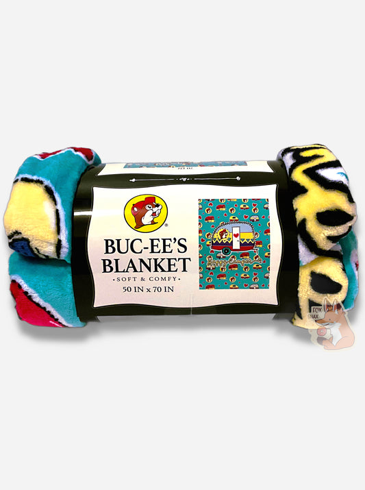 A picture of a soft red, blue, yellow, and white blanket covered in Buc-ee's logos and cartoon campers.  The logo is Buc-ee The Beaver, wearing a red ball cap against a yellow circle background.  In the center is a giant cartoon camper; underneath that, the words HAPPY CAMPER in cursive.  The label reads BUC-EE'S BLANKET *SOFT AND COMFY* 50 IN x 70 IN