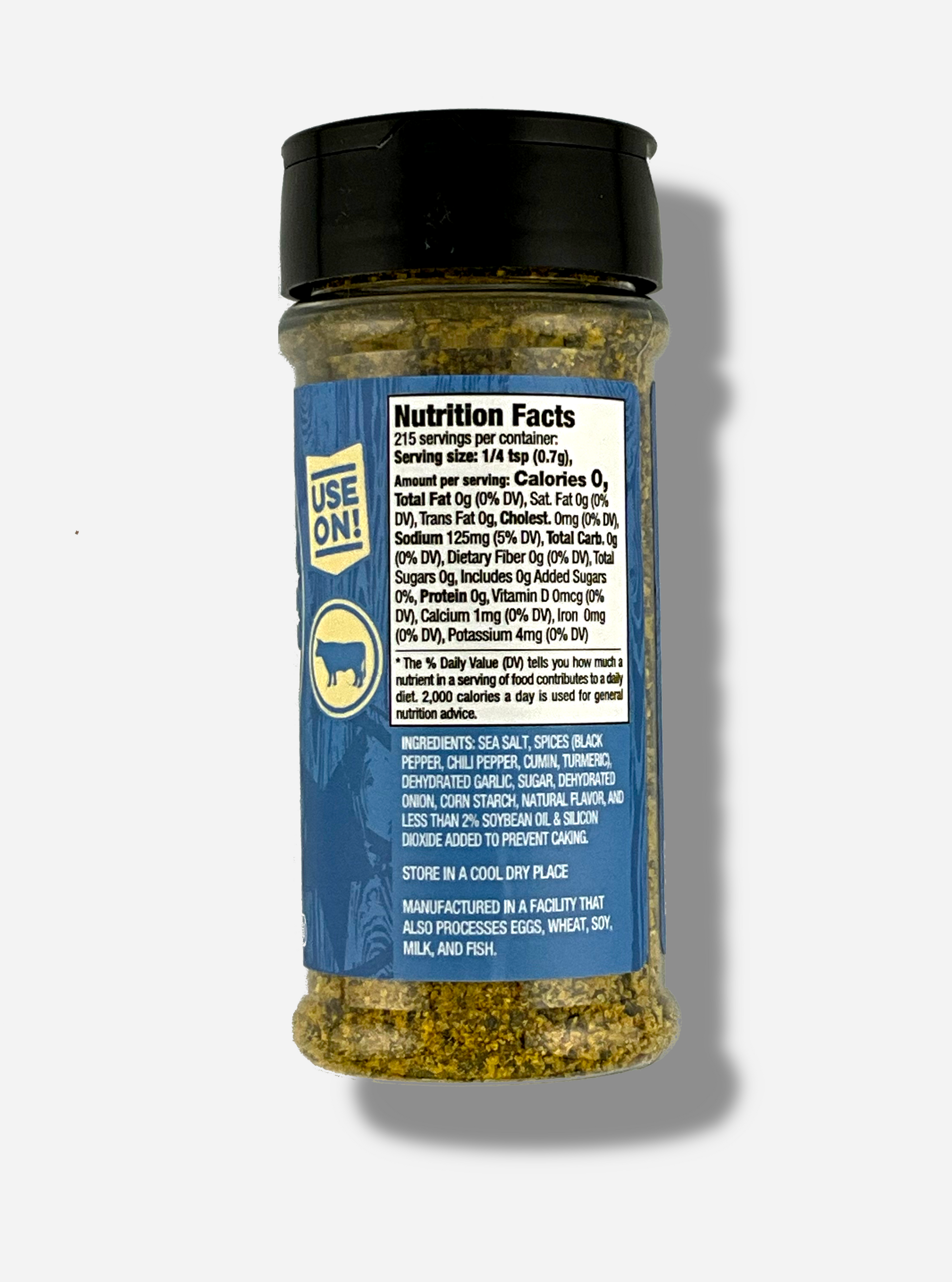 A picture of the back of a container of Texas Round Up Brisket Rub.  The container has a black plastic flip lid, and a clear plastic body.  The spices inside appear grey and black.  The blue label reads USE ON!, and beneath that, there is an outline of a cow.