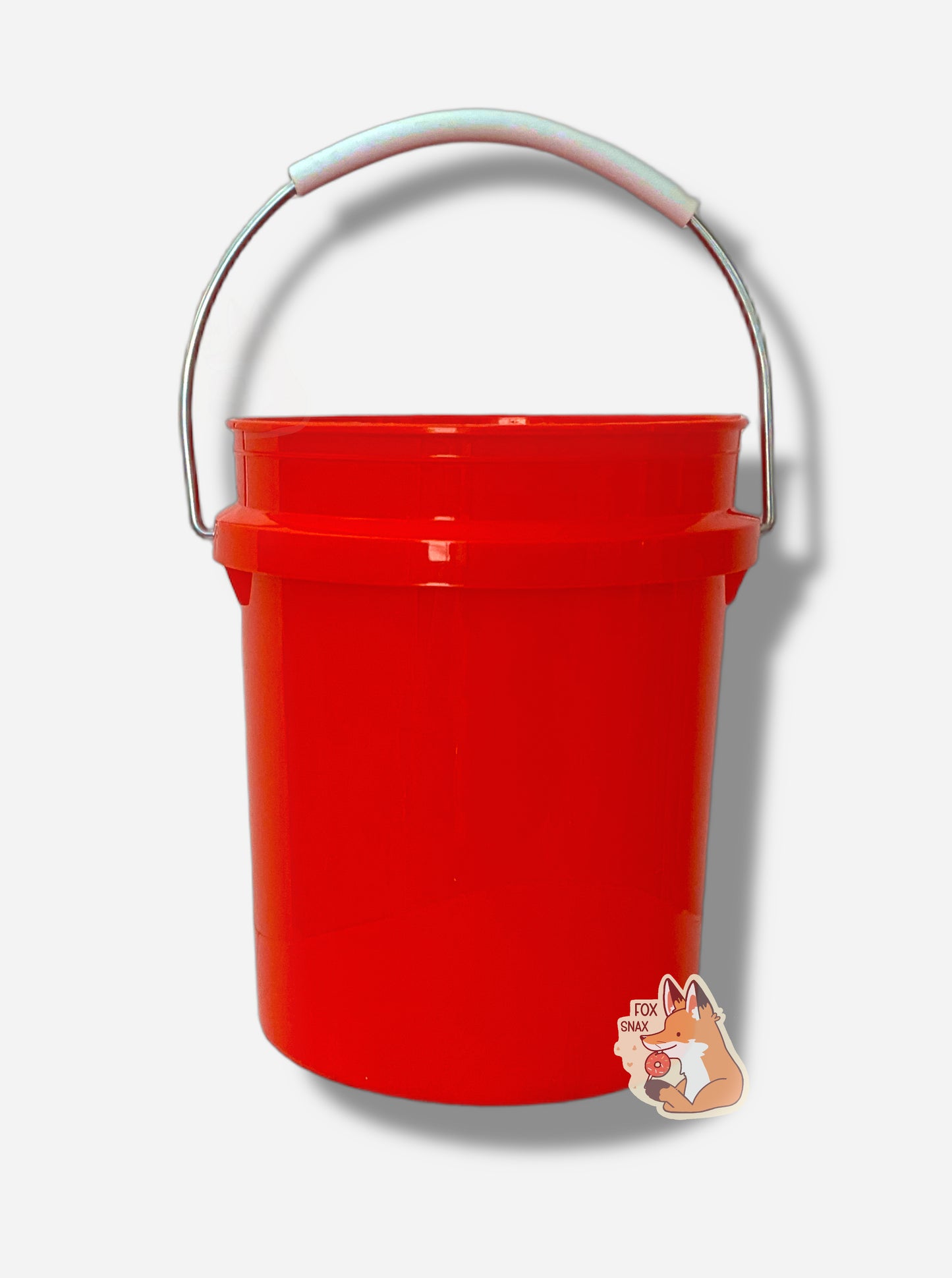 A picture of the back of a small, bright red, miniature bucket.   A metal handle, partially coated in white plastic, is attached to the top of the bucket.