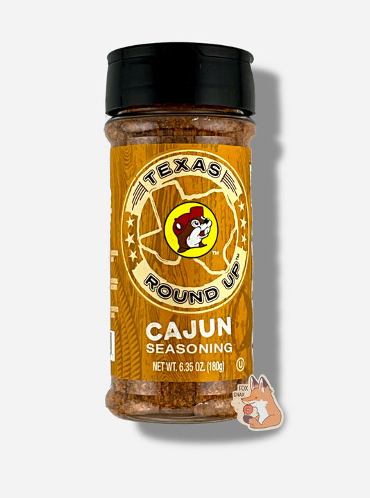 A picture of the front of a container of Texas Round Up Cajun Seasoning.  The container has a black plastic flip lid, and a clear plastic body.  The spices inside orange and black.  The label reads TEXAS ROUND UP, with an outline of the state of Texas, with a picture of Buc-ee The Beaver in the middle.  Beneath that, the red label reads in white text, Cajun Seasoning.  Net Wt 6.35 Oz (180g).