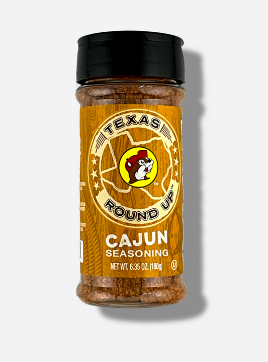 A picture of the front of a container of Texas Round Up Cajun Seasoning.  The container has a black plastic flip lid, and a clear plastic body.  The spices inside orange and black.  The label reads TEXAS ROUND UP, with an outline of the state of Texas, with a picture of Buc-ee The Beaver in the middle.  Beneath that, the red label reads in white text, Cajun Seasoning.  Net Wt 6.35 Oz (180g).